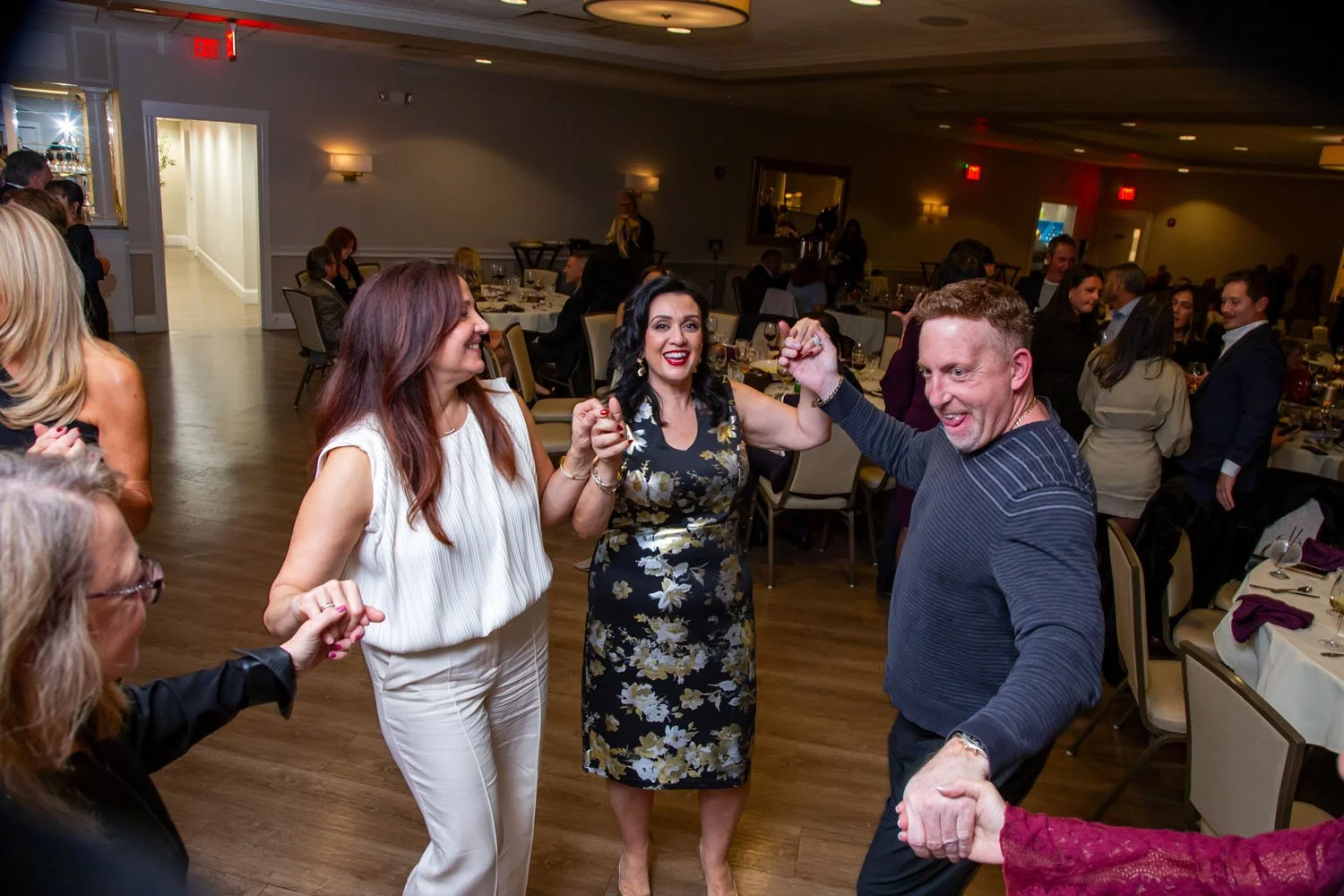 People dancing and celebrating at a banquet hall with round tables set for dinner