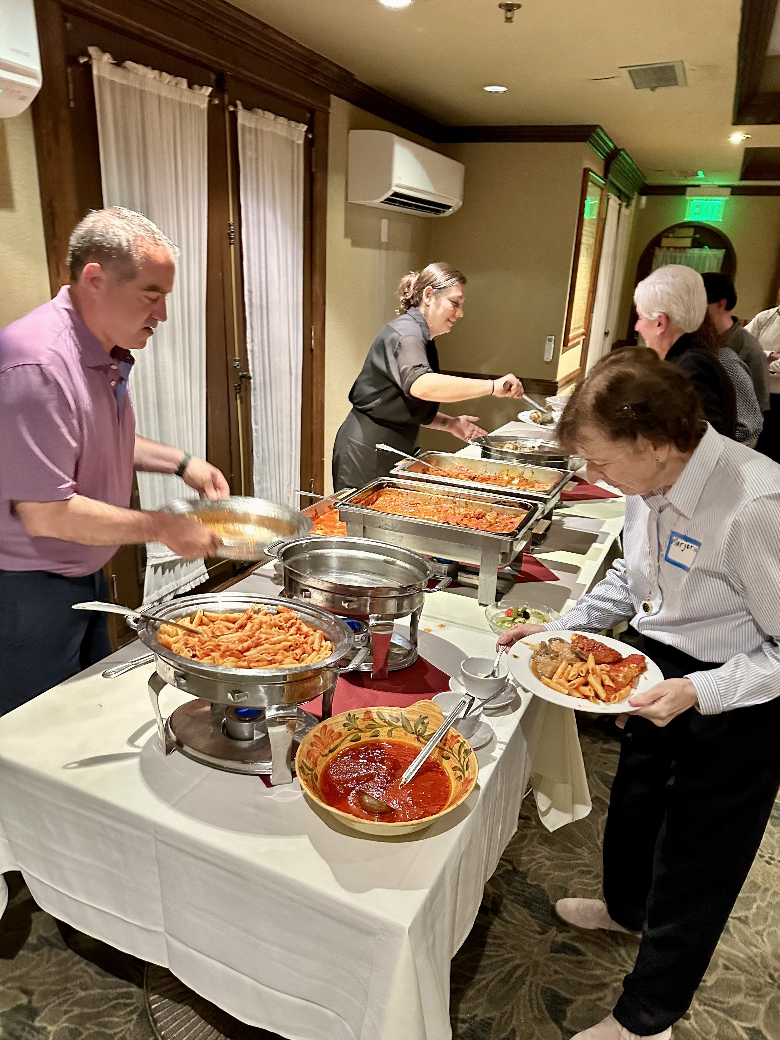 Buffet table with people serving pasta and sauce in a banquet hall.