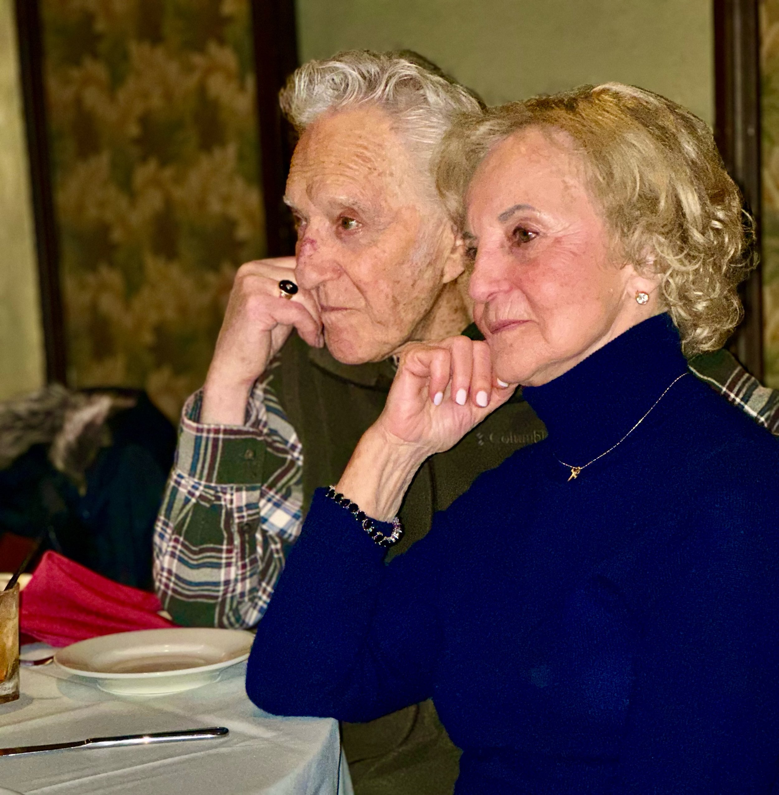 Elderly couple sitting at a dining table with thoughtful expressions.