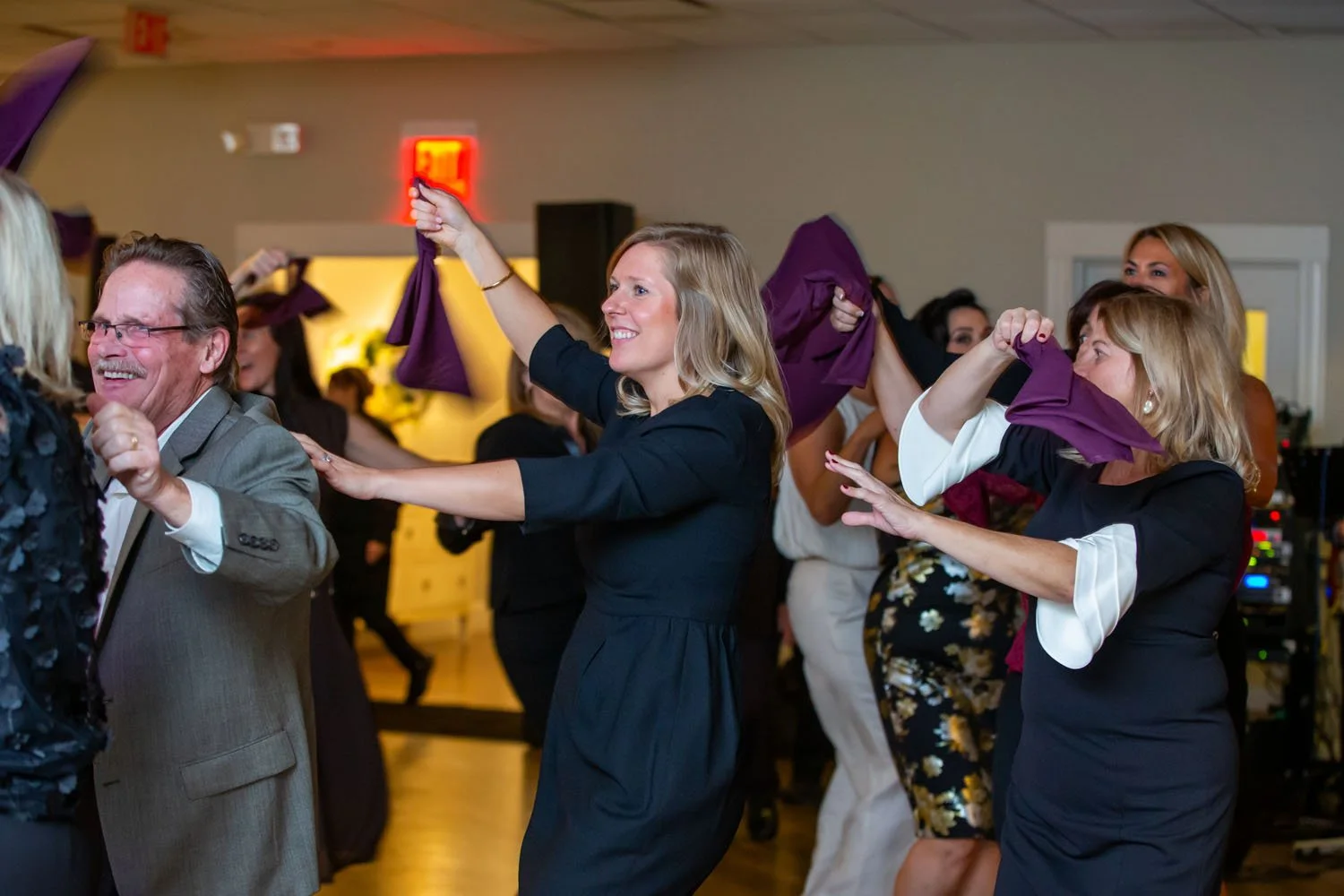 People enjoying a dance at a celebration, holding purple napkins, with a joyful atmosphere.
