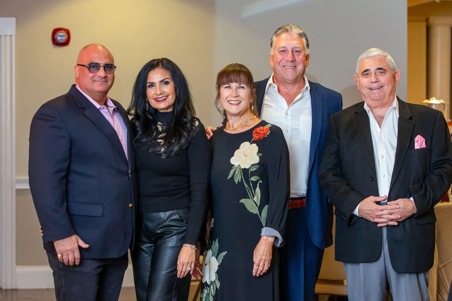 Five adults standing together at an indoor event, smiling at the camera, dressed in business or semi-formal attire.