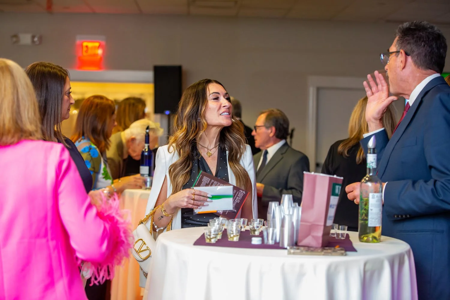 A group of people, mostly women, are socializing around a round table at a formal event or conference, engaging in conversation.