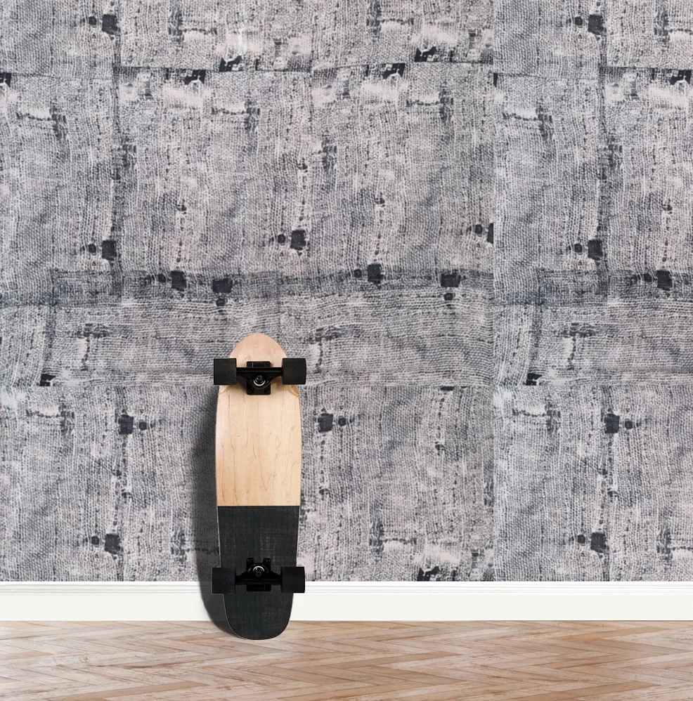 A wall with Indigo Akan wallpaper in monochromatic tones installed, with a skateboard leaning against the wall..