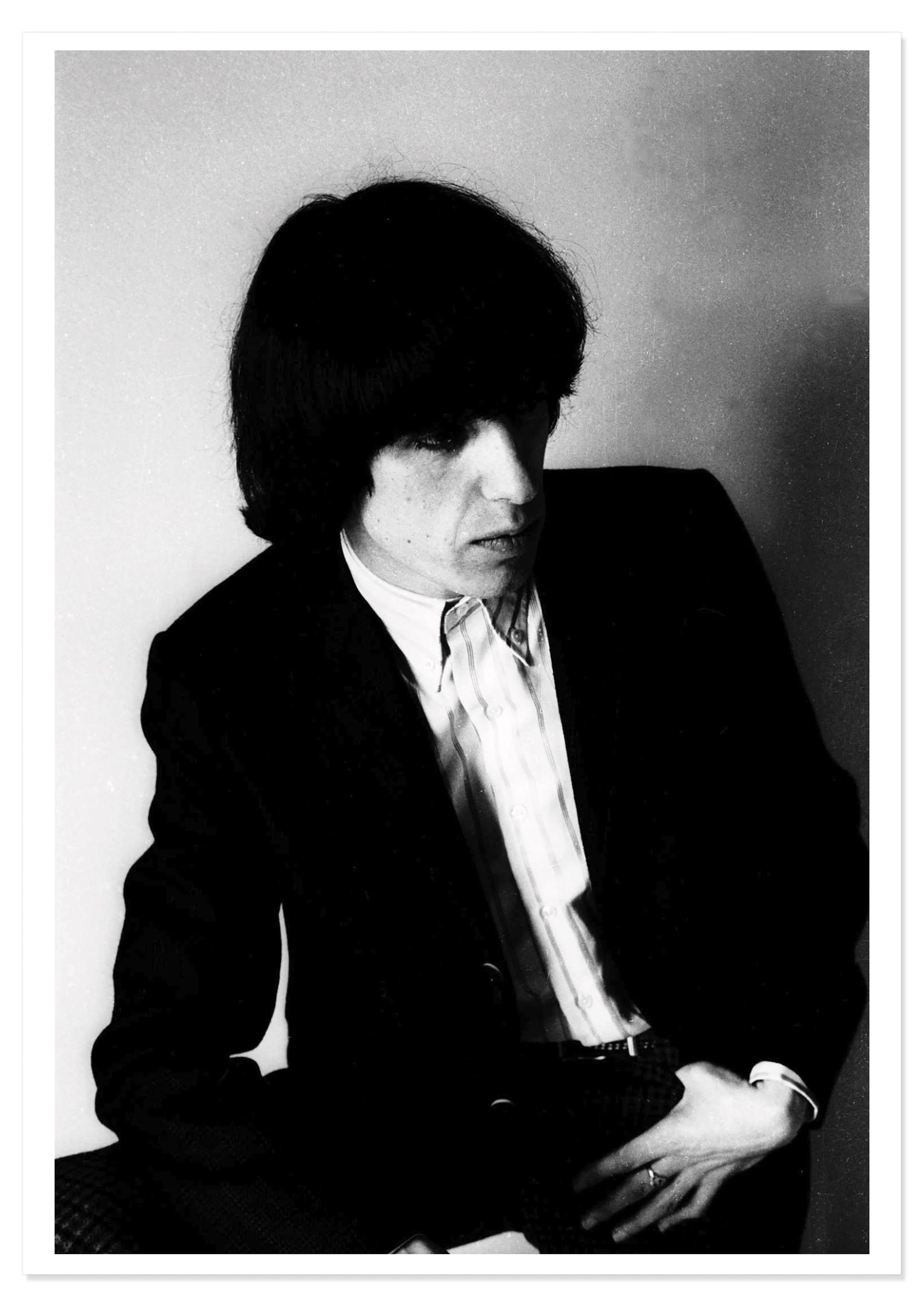 Print with drop shadow showing black and white head and shoulders portrait image of Bill Wyman of the Rolling Stones wearing a black jacket and white shirt.