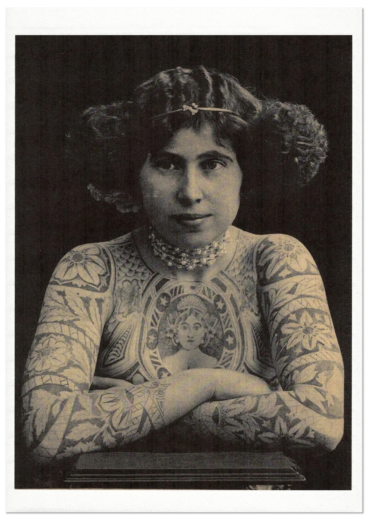 Print of vintage photograph of a woman's upper body covered in tattoos and with a pearl choker.