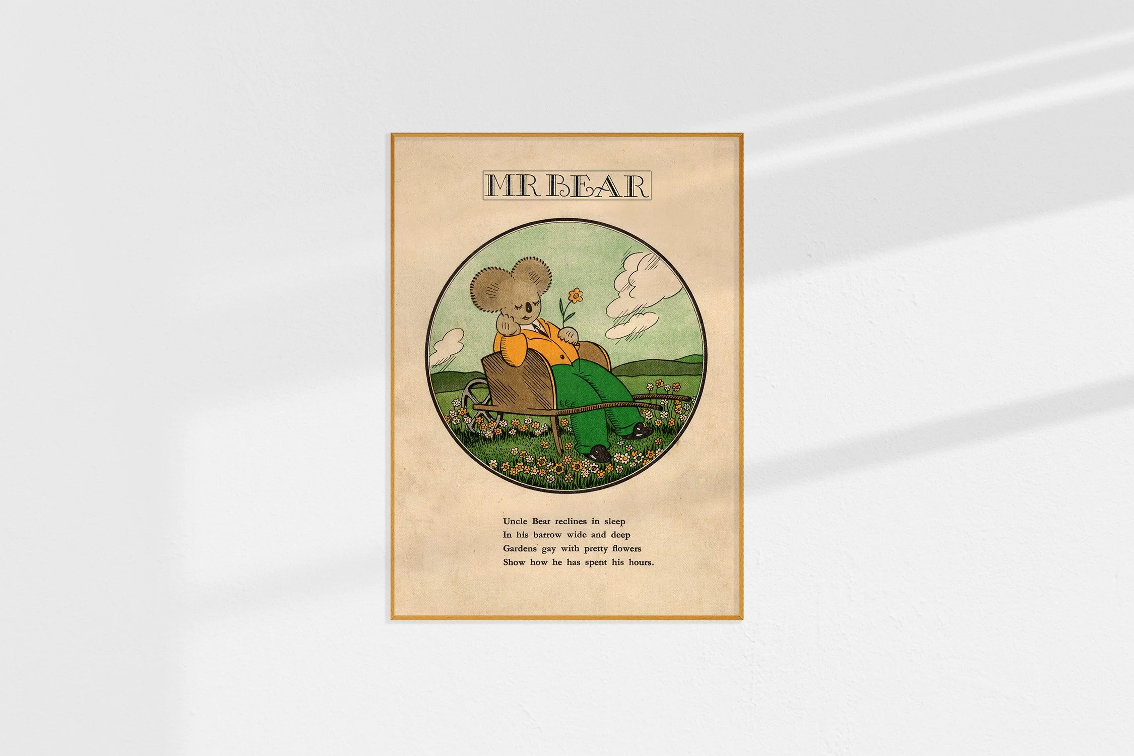 A framed Oz print of a koala Mr Bear in a roundel snoozing in a wheelbarrow with a yellow flower.