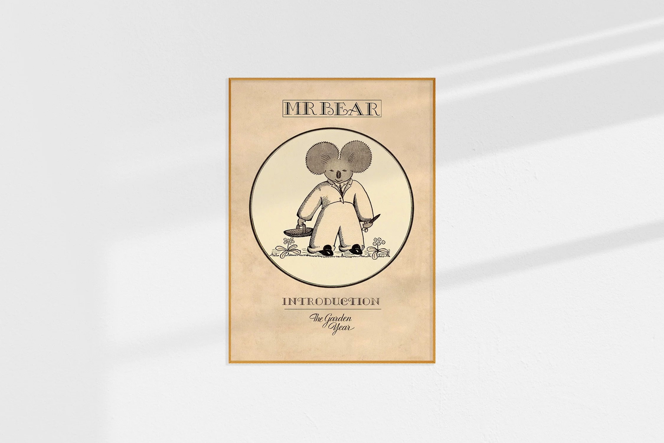 A framed Oz print with a koala Mr Bear in a roundel with a basket and a pair of scissors ready to cut flowers.