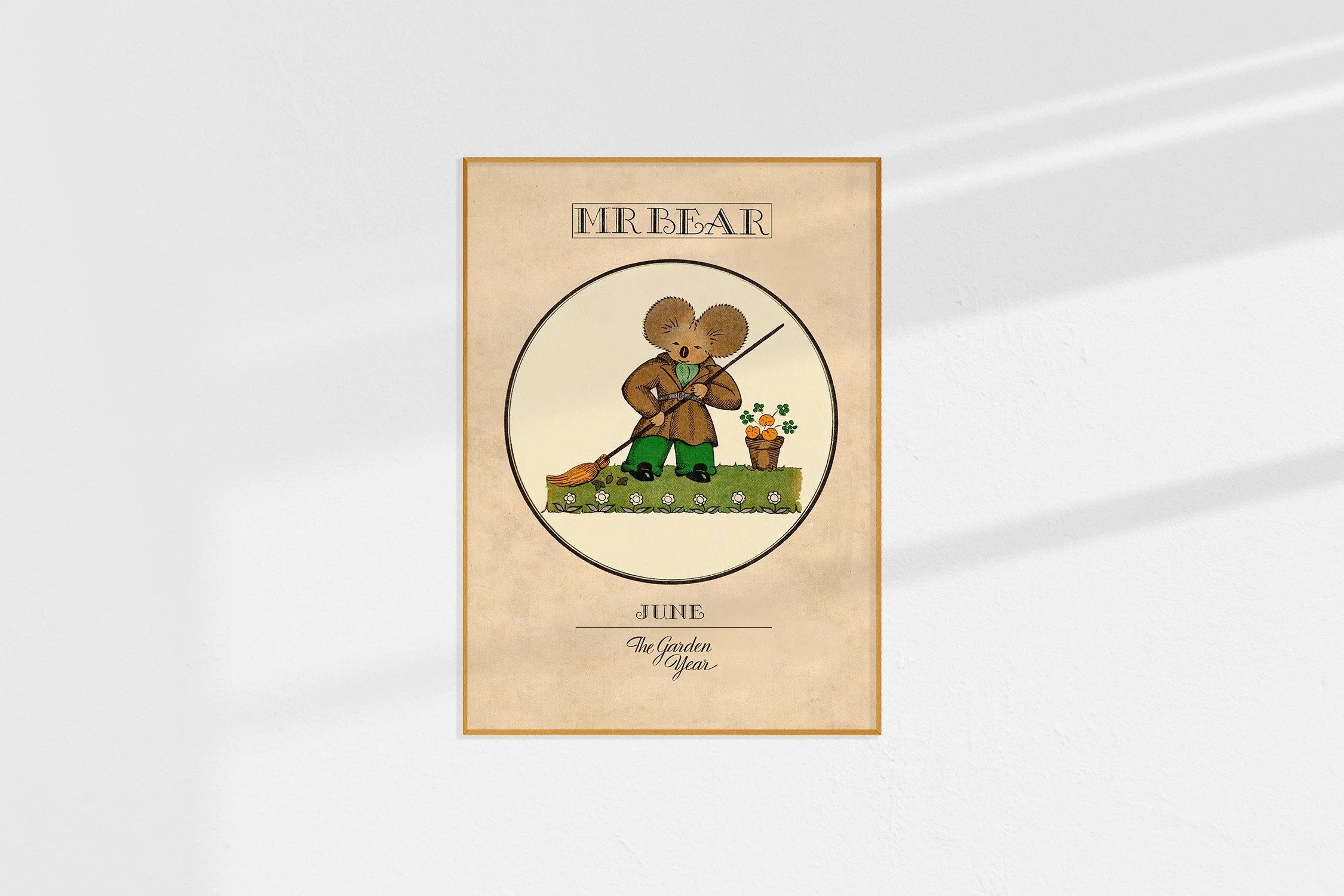 A framed Oz print with a koala Mr Bear in a roundel dressed in a coat sweeping leaves.