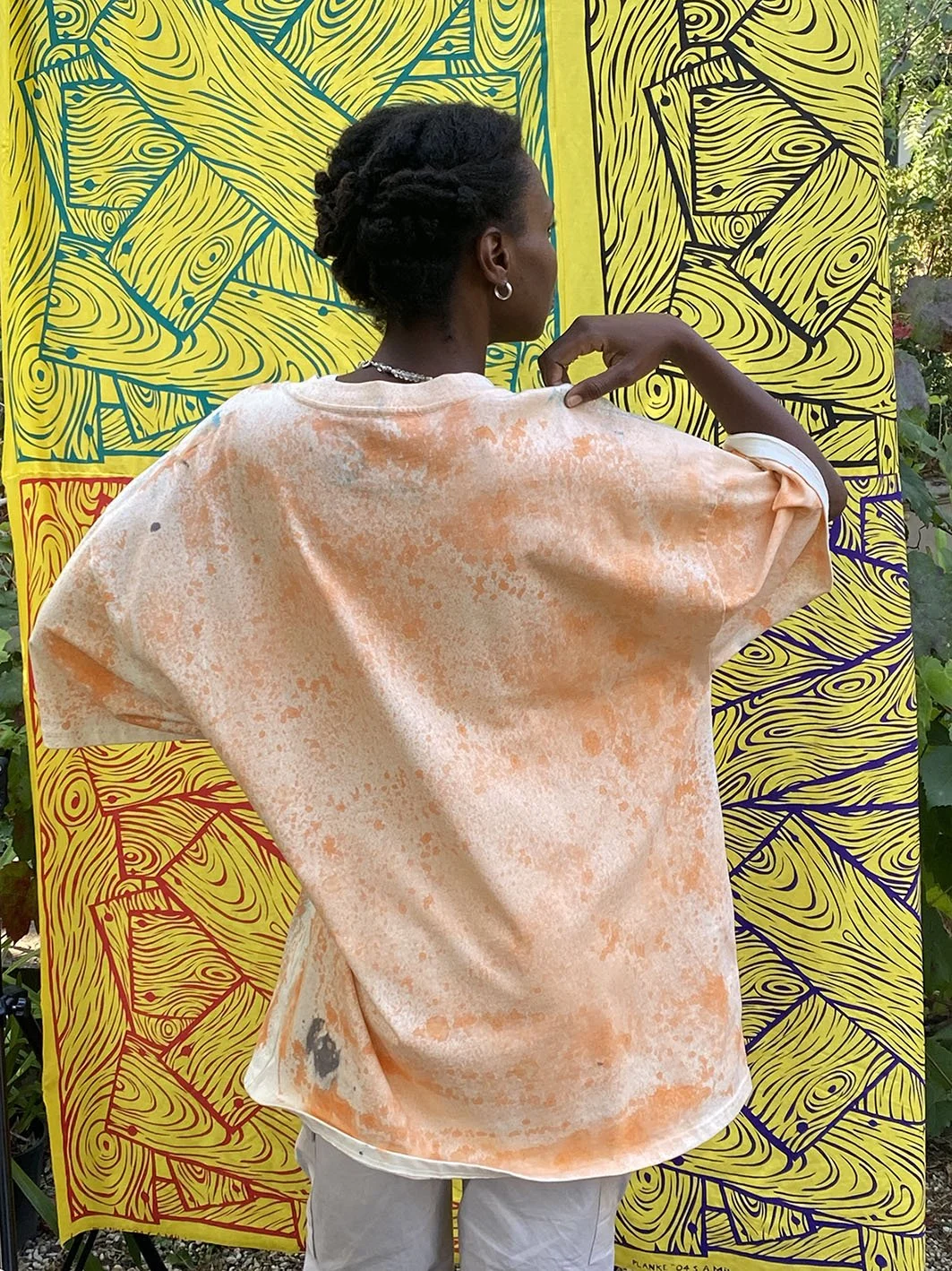 Model shows back view of heavy weight short sleeved treated tshirt against a backdrop of woodgrain fabric.