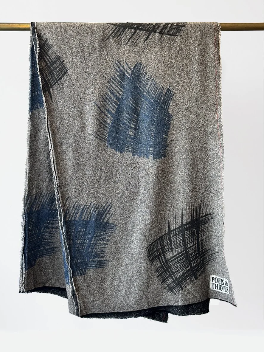 An image of the front of a wool blend throw with flymo abstract squares in black and blue and a decorative red scalloped edge stitch.