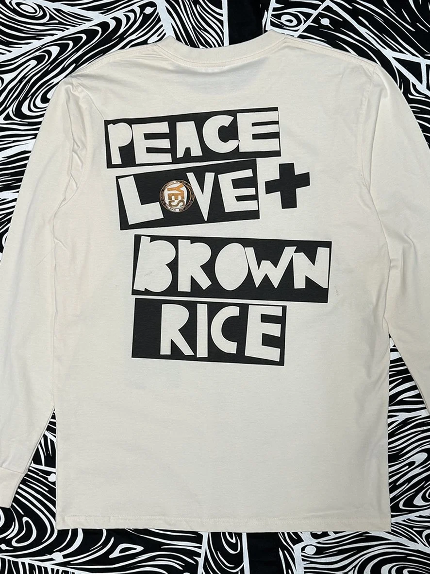 Back view of a natural long sleeved tee with a large black Peace Love and Brown Rice logo in the centre.