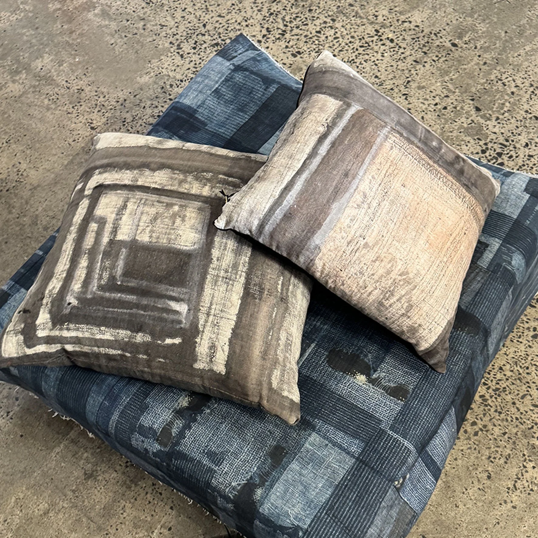 Two artist original mudcloth large linen cushions on an ottoman covered with indigo denim..