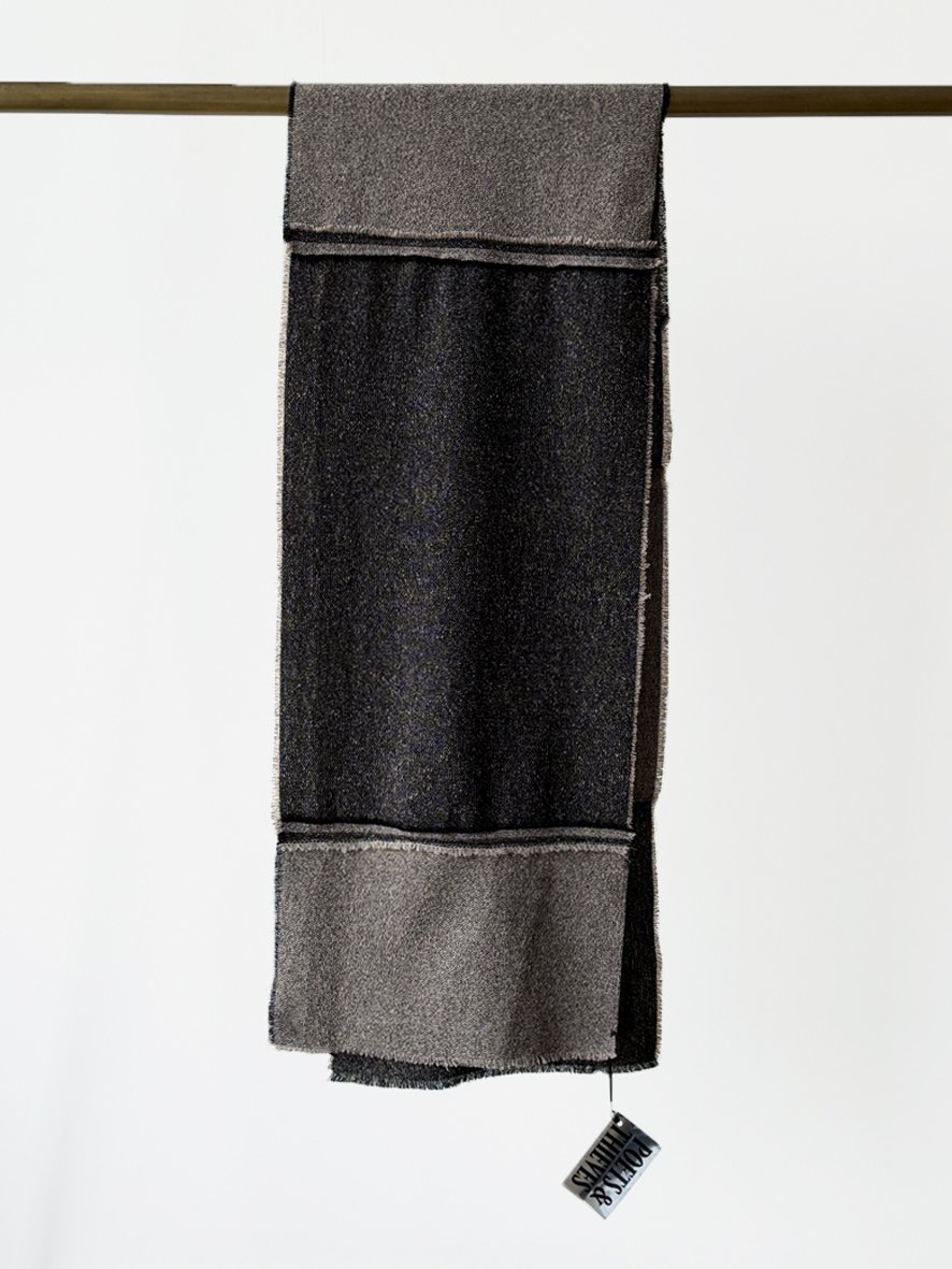An image of the back of a long slim wool blend scarf with reversed patches and frayed edging in black and charcoal.