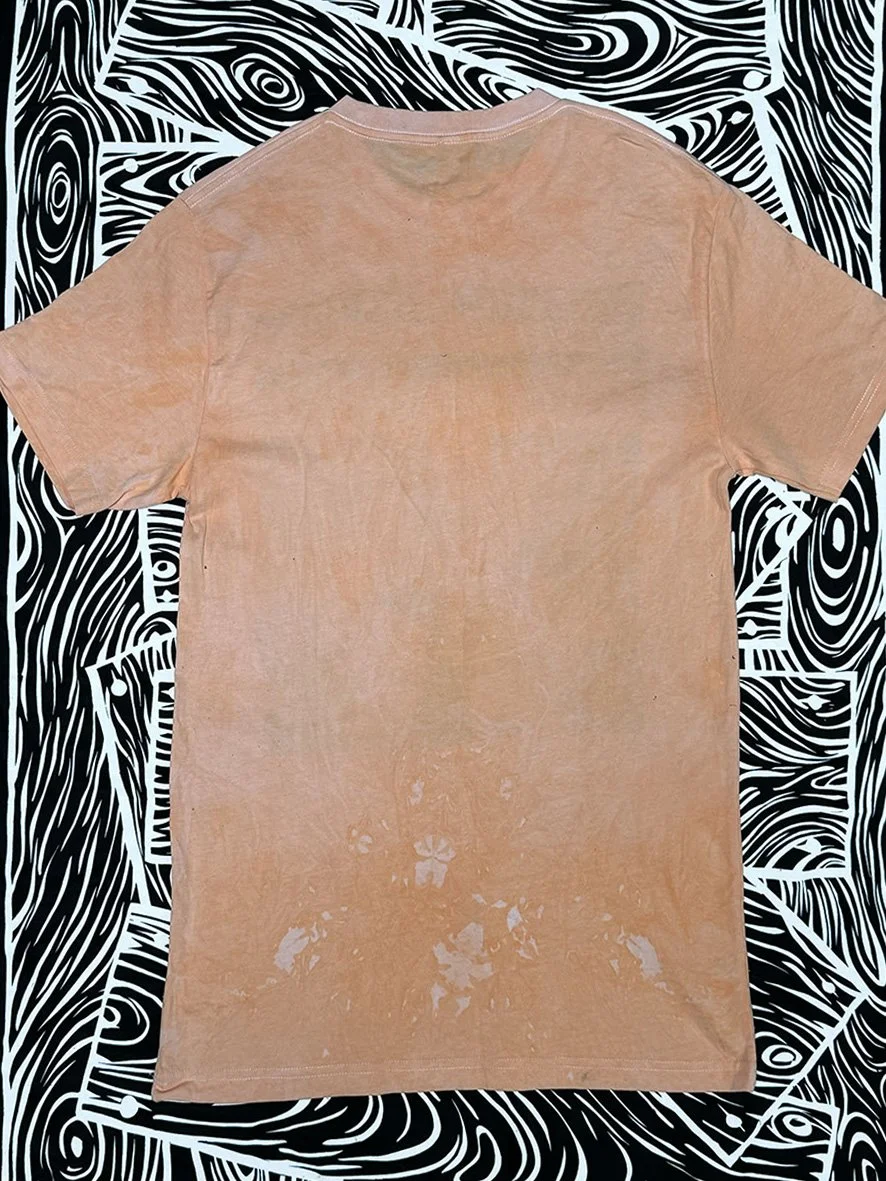Back view of a treated orange tshirt with black and white woodgrain fabric behind.