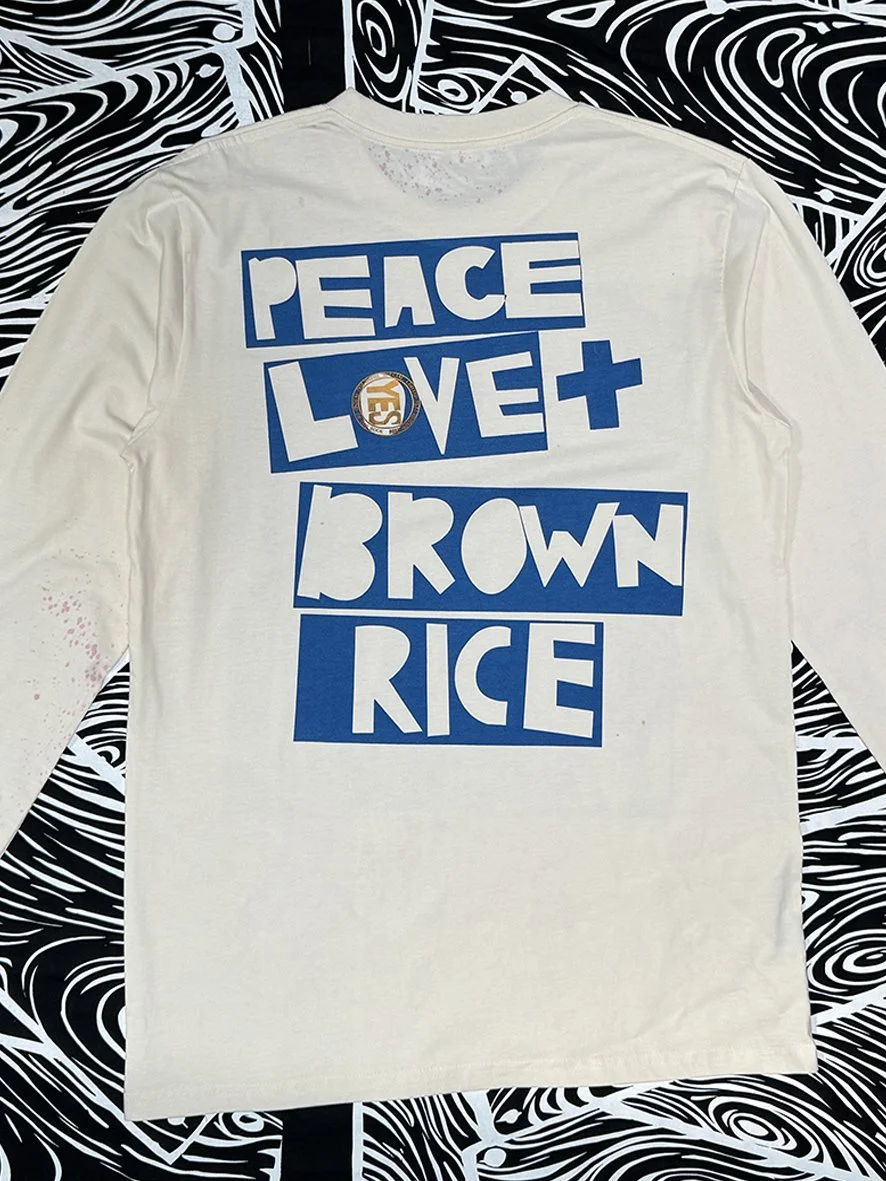 Back view of a natural long sleeved tee with a large blue Peace Love and Brown Rice logo in the centre.