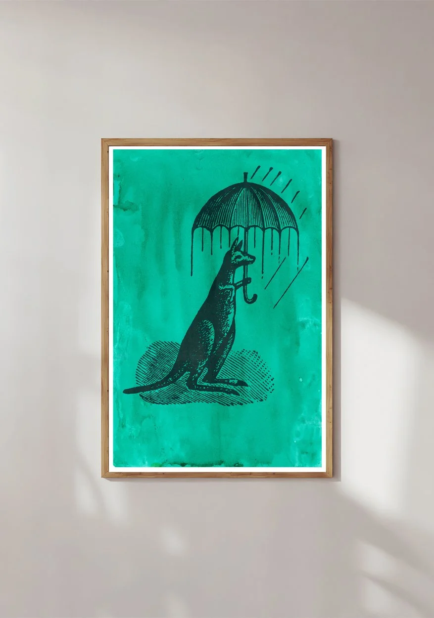Framed print of a kanga with an umbrella and with an artistic green gouache background by Hoponit Studio.