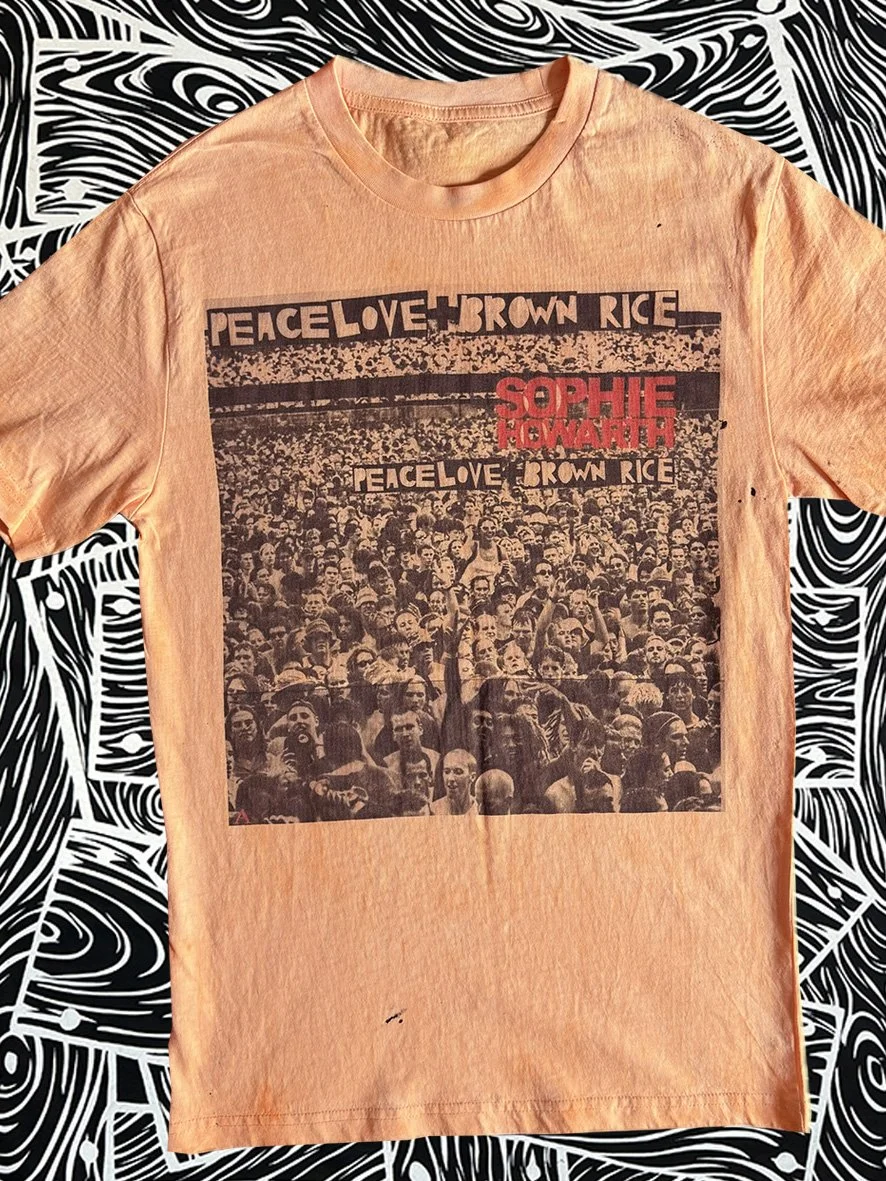 Front view of oxidised orange tee with a Peace Love and Brown Rice print and with black and white woodgrain fabric behind.