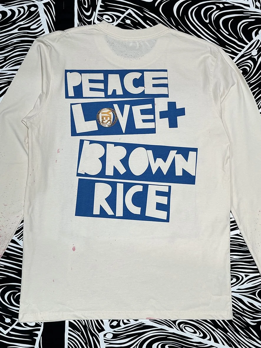 Back view of natural long sleeved tee with a large blue Peace Love and Brown Rice logo in centre.