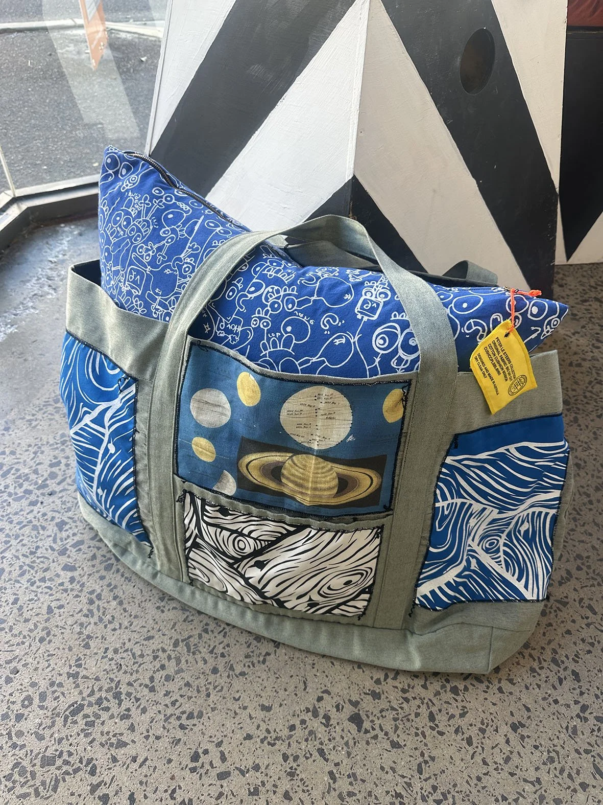 Oversized canvas bag with astrology and woodgrain patches and with a blue Peter Le Steers rabbit cushion inside.
