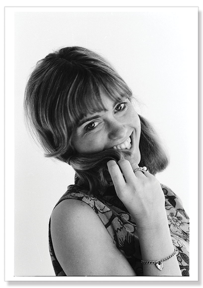Black and white close-up portrait photograph of Olivia Newton-John's face, with a girlish pigtail look.  Print shows borders and drop shadow.