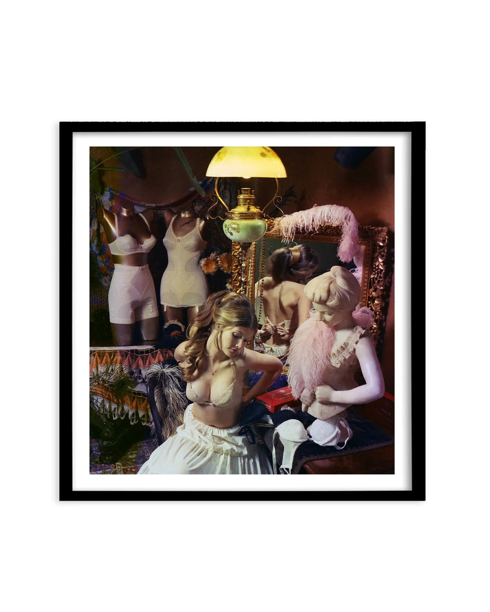 Black framed photographic image of a girl in lingerie and surrounded by other lingerie and feathers in a boudoir.