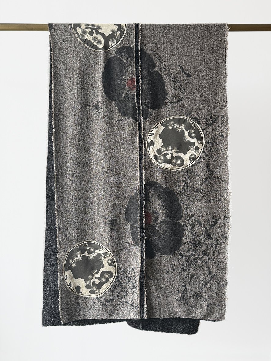 An image of the front of a long slim wool blend and silk throw with frayed edging in black poppies and cream silk Japanese flowers.
