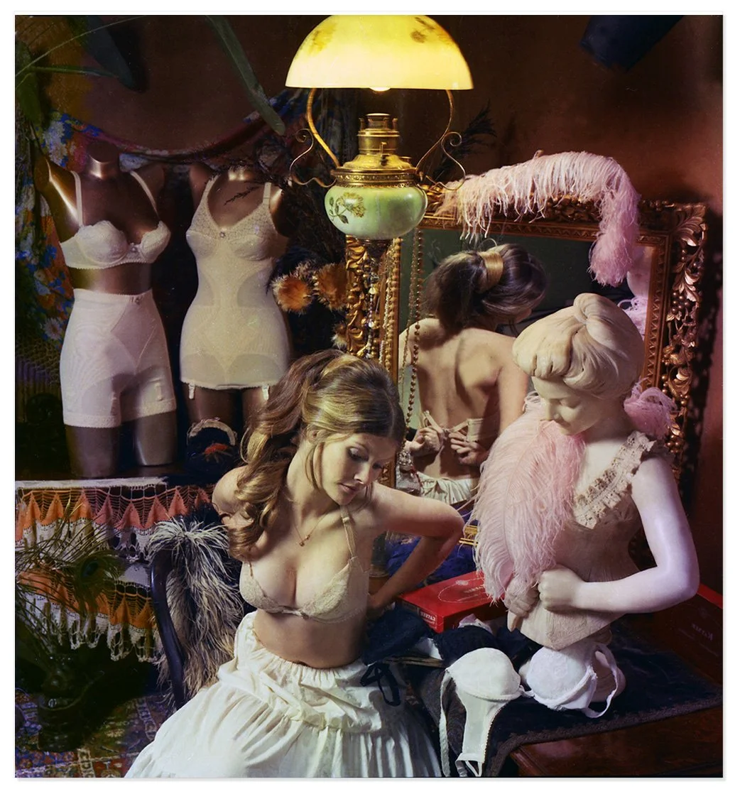 A photographic image with a girl in lingerie and surrounded by other lingerie and feathers in a boudoir with a drop shadow.