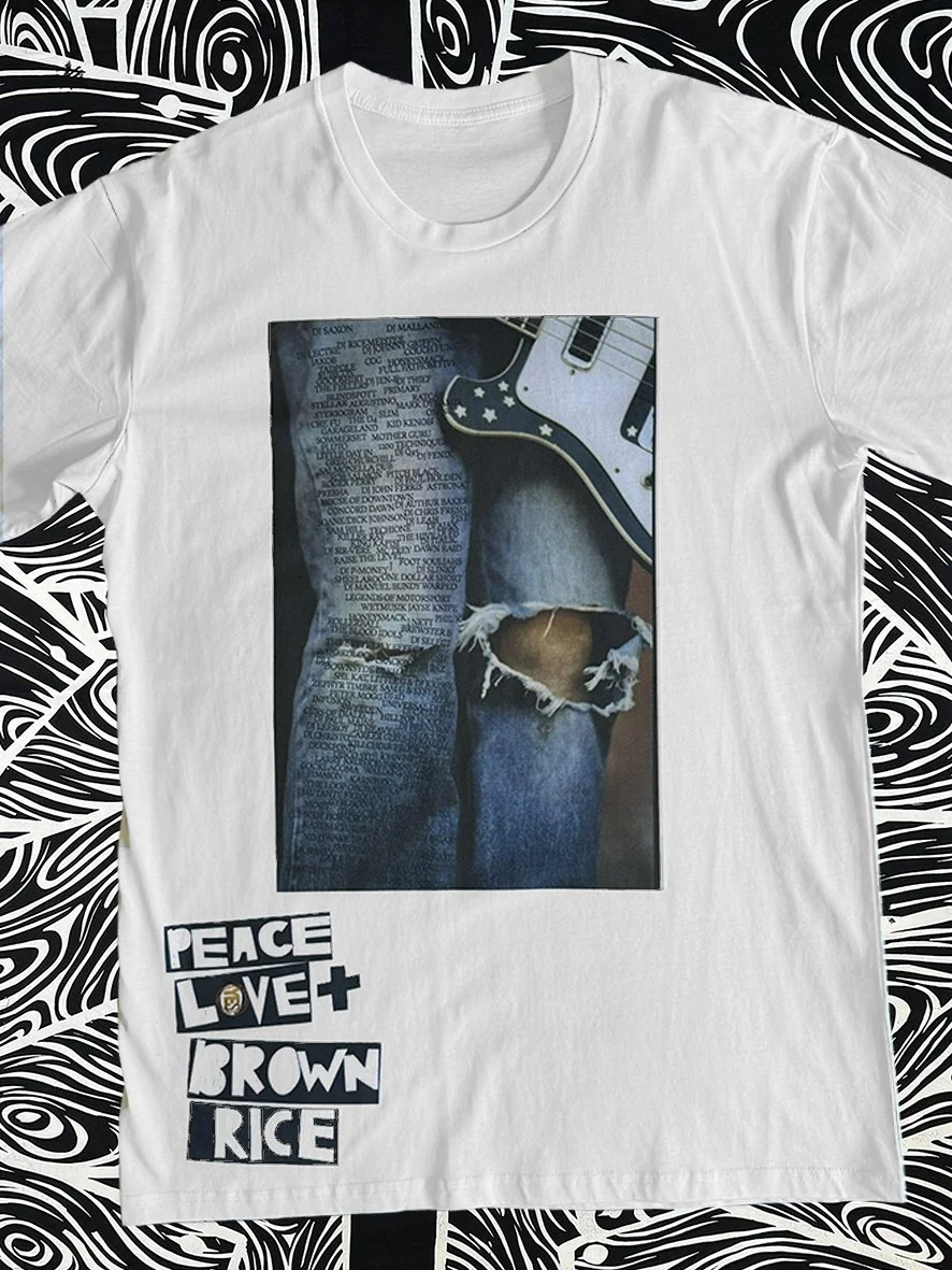 Front view of white tee with a Peace Love and Brown Rice print and with black and white woodgrain fabric behind.