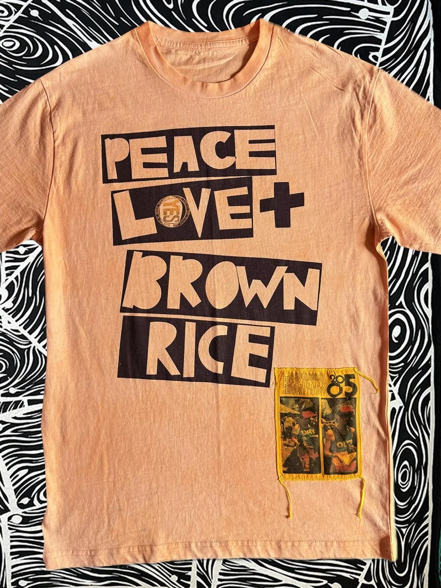 Front view of oxidised orange Peace Love and Brown Rice tee with a small patch and with black and white woodgrain fabric behind.