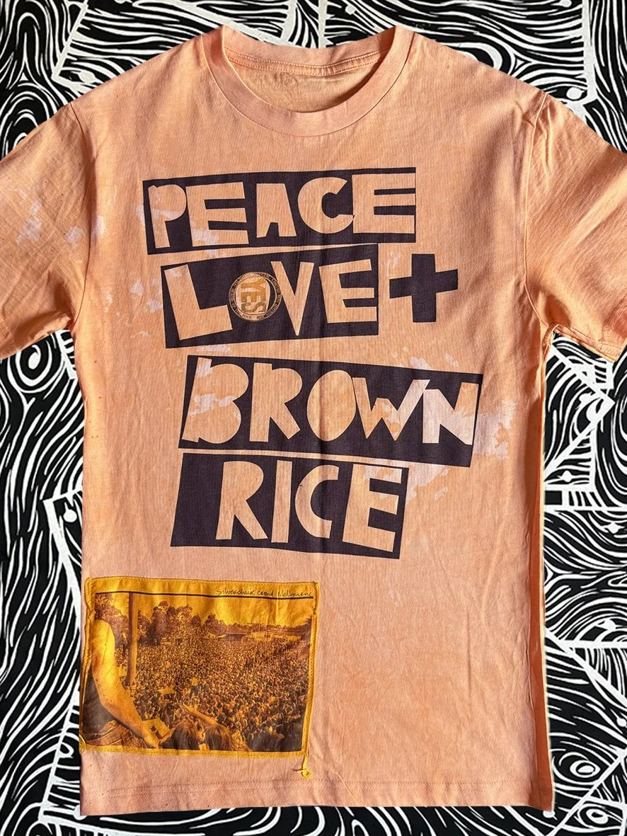 Front view of oxidised orange tee with a Peace Love and Brown Rice print and Silverchair patch and with black and white woodgrain fabric behind.