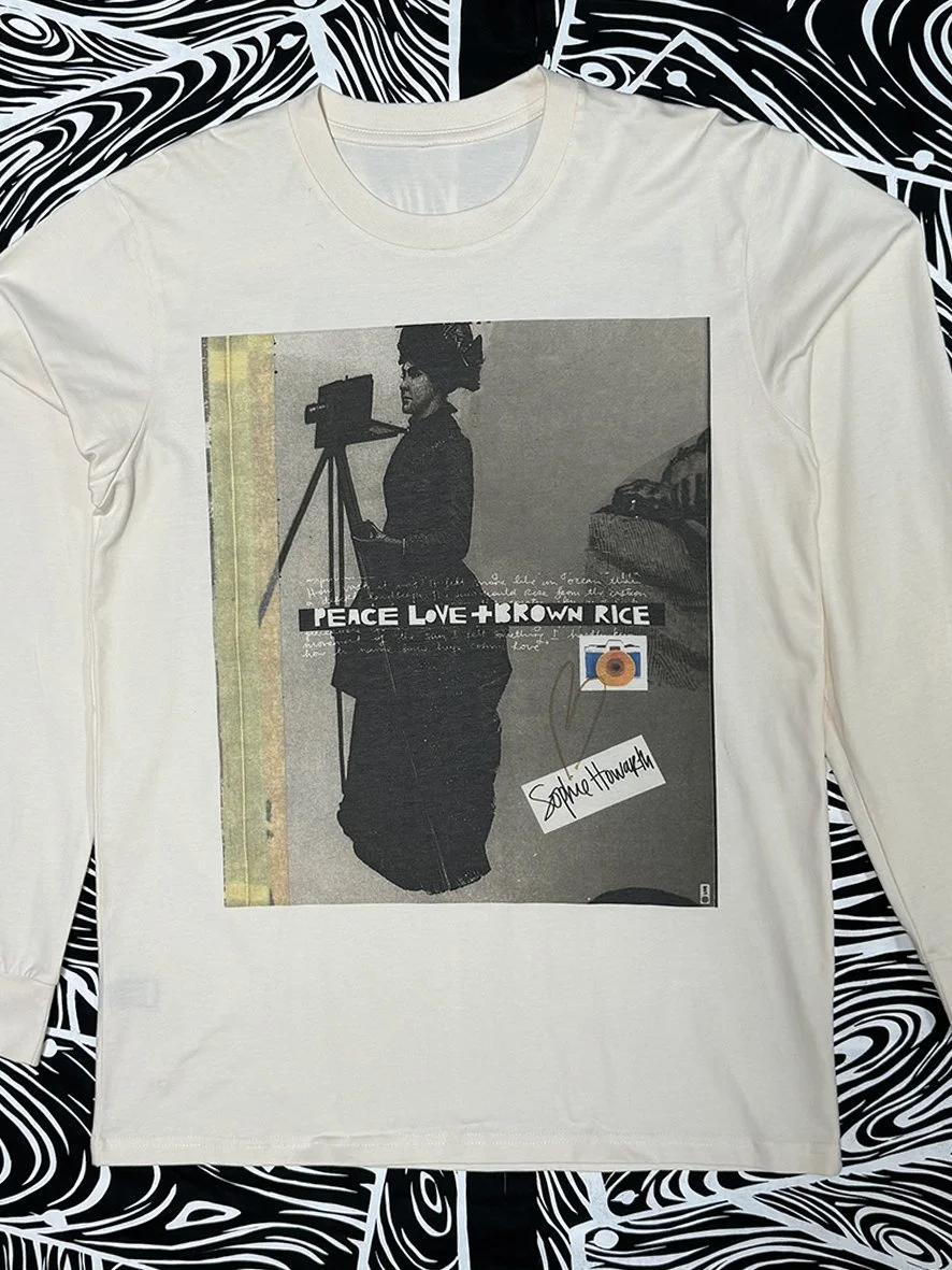 Front view of long sleeved natural tee with a sepia image of a woman photographer with a tripod camera and Peace Love and Brown Rice overlaid.