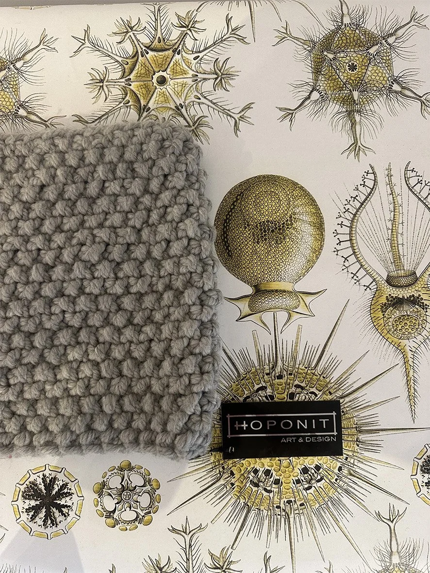 Folded over knitted snood (neck scarf) photographed on Haeckel wallpaper by Hoponit Studio.