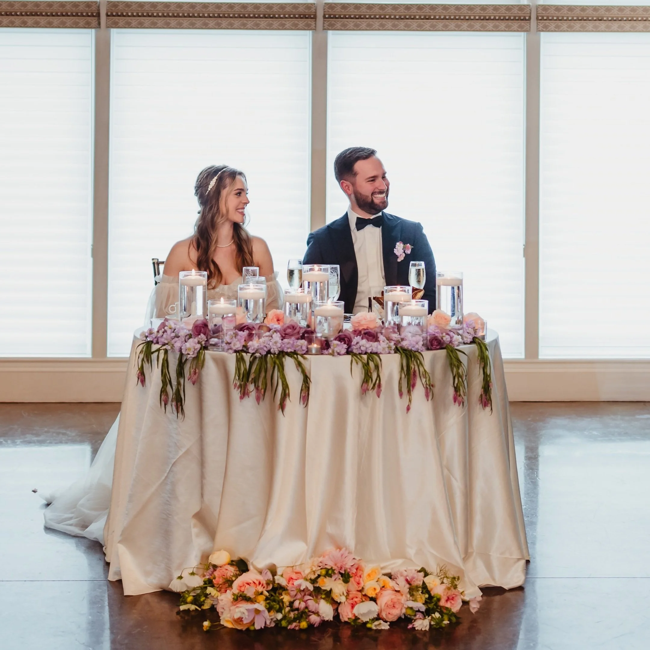 Bride and groom sitting at a decorated wedding table with candles and flowers.