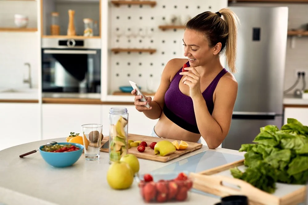 young-happy-athletic-woman-eating-fruit-while-text-messaging-mobile-phone-kitchen-mod.jpg