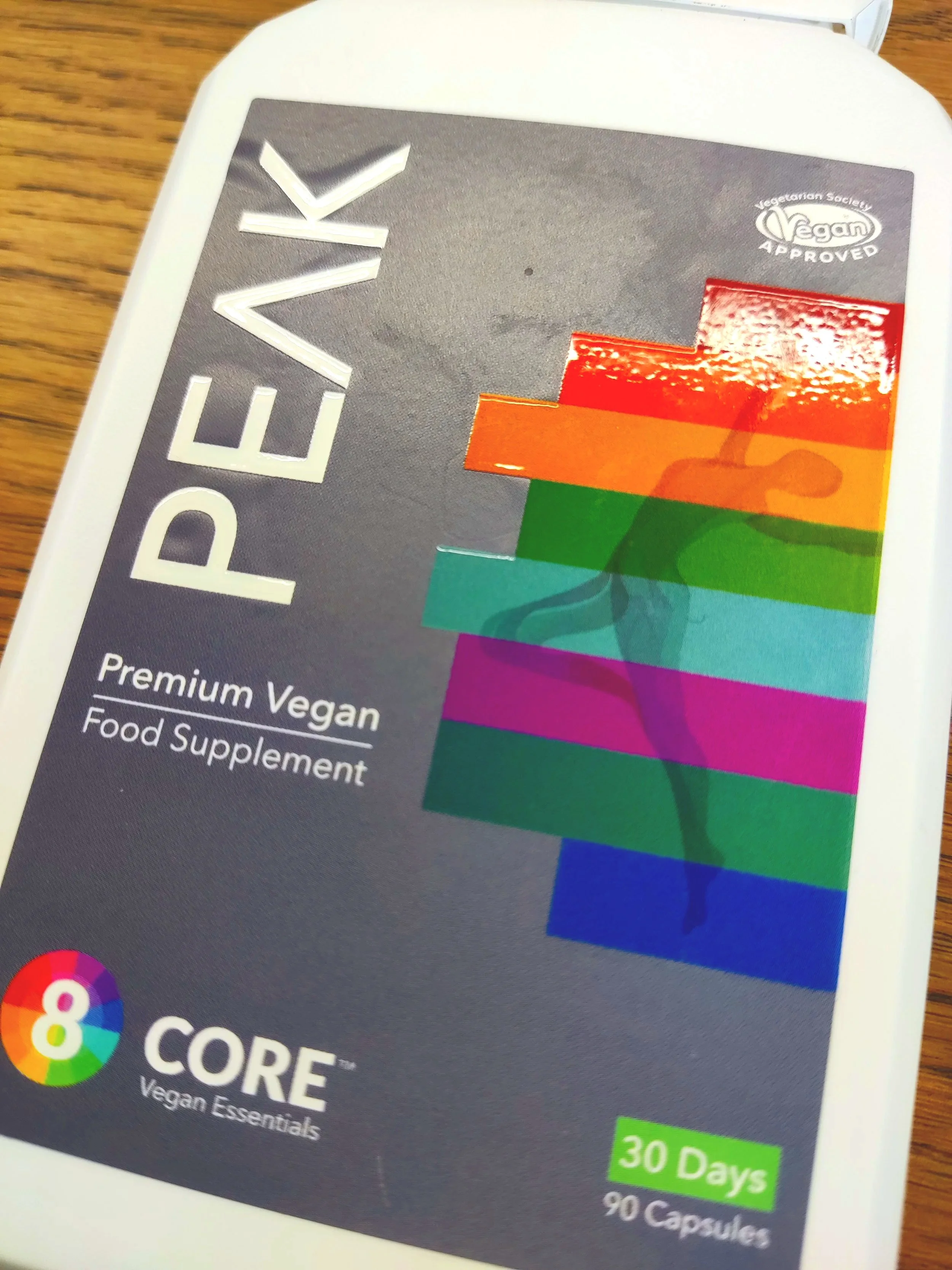 Package of vegan dietary supplement capsules with a colorful rainbow design and label indicating 30 days supply, with 90 capsules inside.