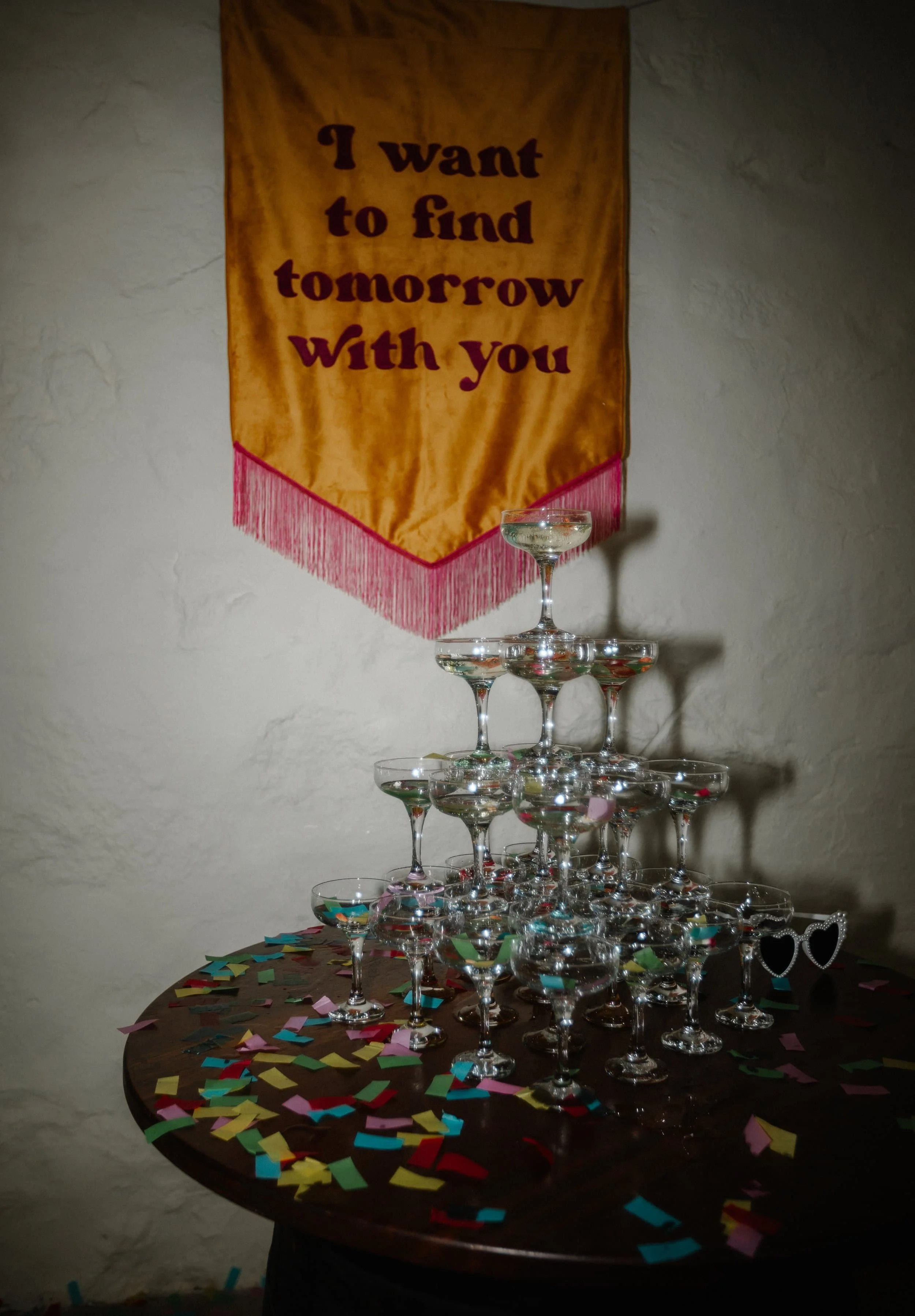 A champagne tower sits on confetti beneath a banner that reads, I want to find tomorrow with you.