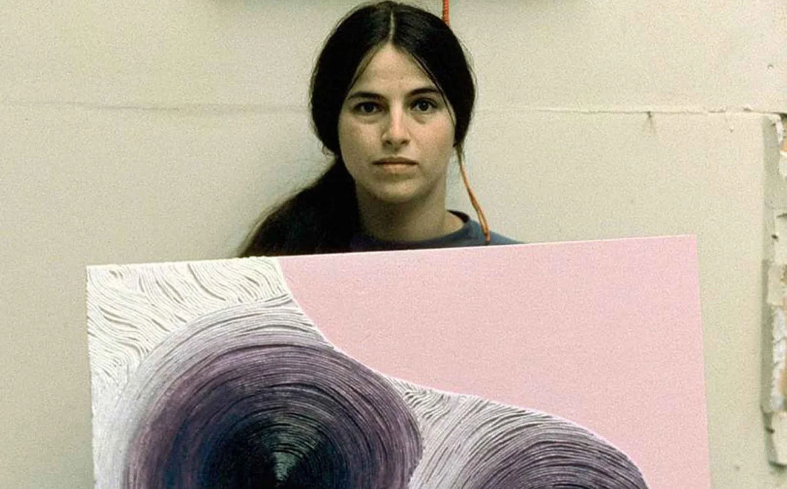 Retrato de Eva Hesse en su estudio sosteniendo una obra, con el titular «La niña que llegó en tren expone en el MoM