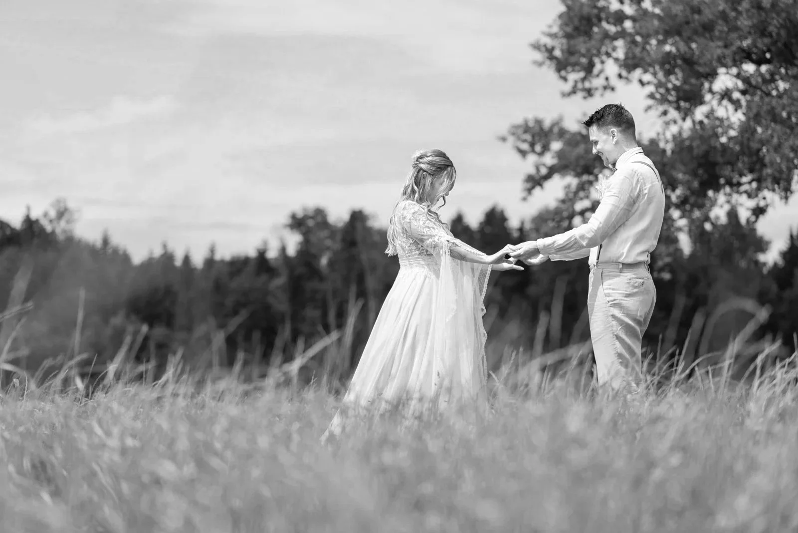 Ein Brautpaar hält sich an einer Wiese im Freien bei einem Fotoshooting an den Händen, schwarz-weiß Bild.
