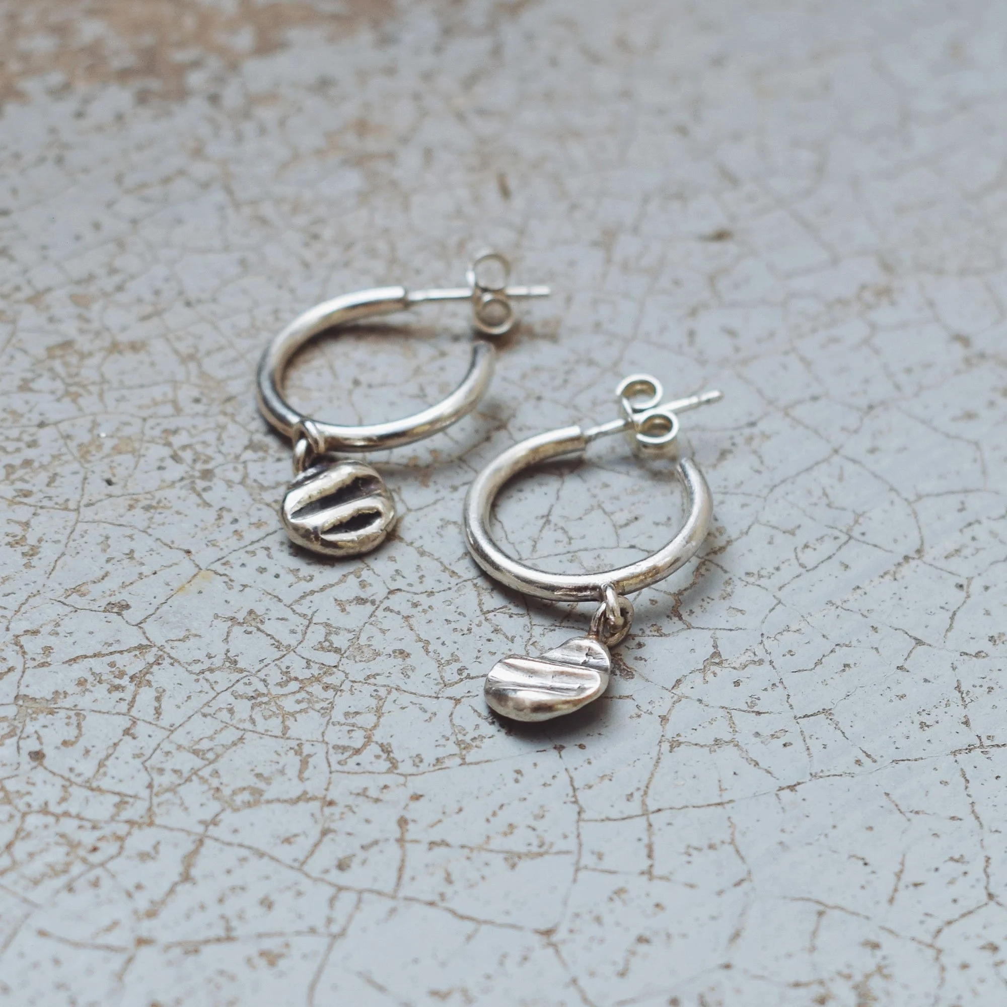 Organic sterling silver hoop earrings with irregular shell-imprinted charms, handmade recycled silver jewelry with a natural coastal aesthetic.