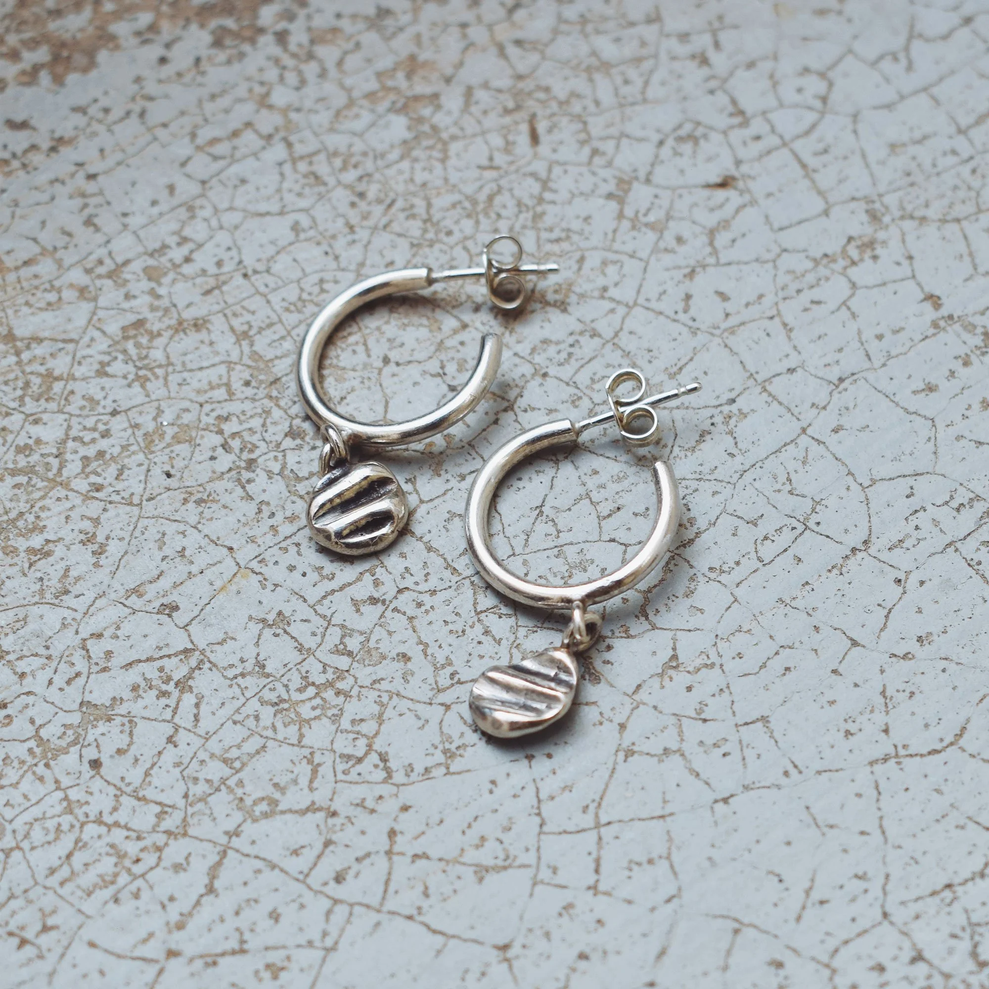 Handmade minimalist silver hoop earrings on a textured background, recycled sterling silver 925 jewelry with sea shell-inspired details.