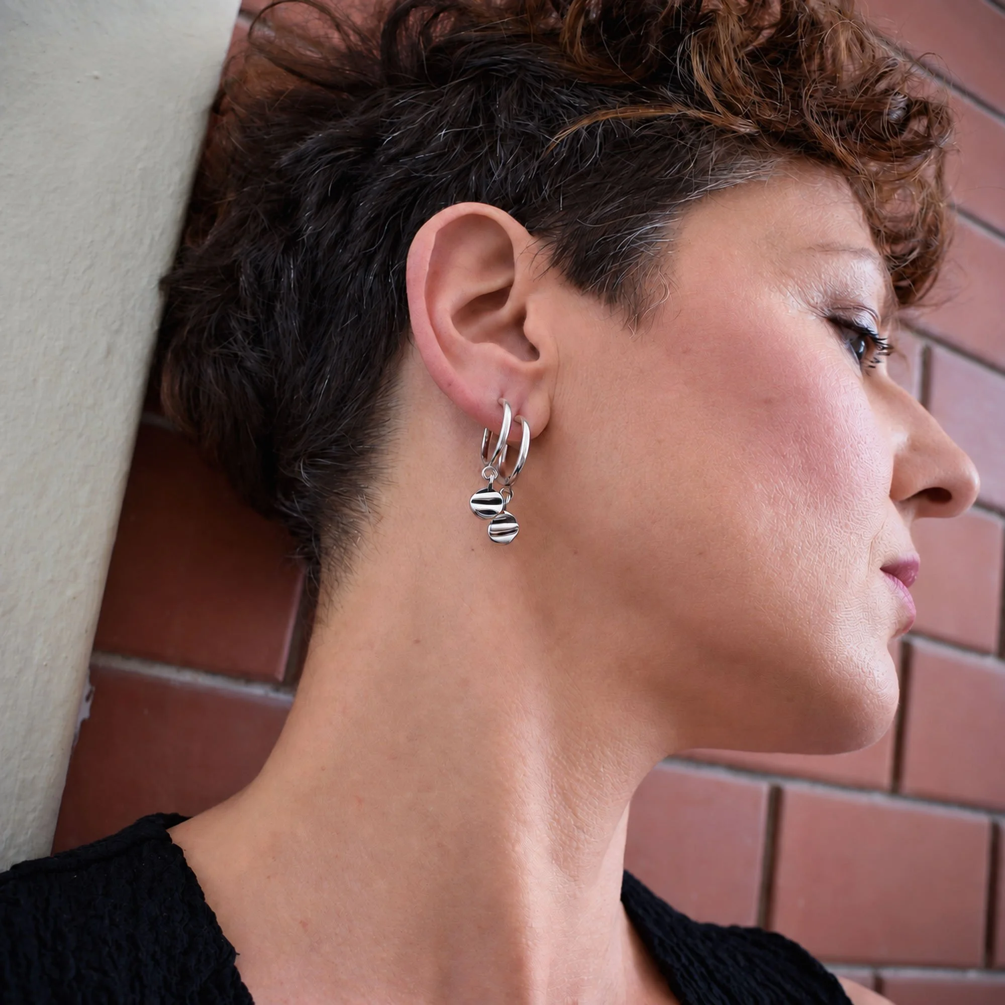 Model wearing handmade sterling silver 925 hoops with organic shell texture charms, minimalist artisan earrings inspired by summer and the sea. Perfect for your ear stacks.