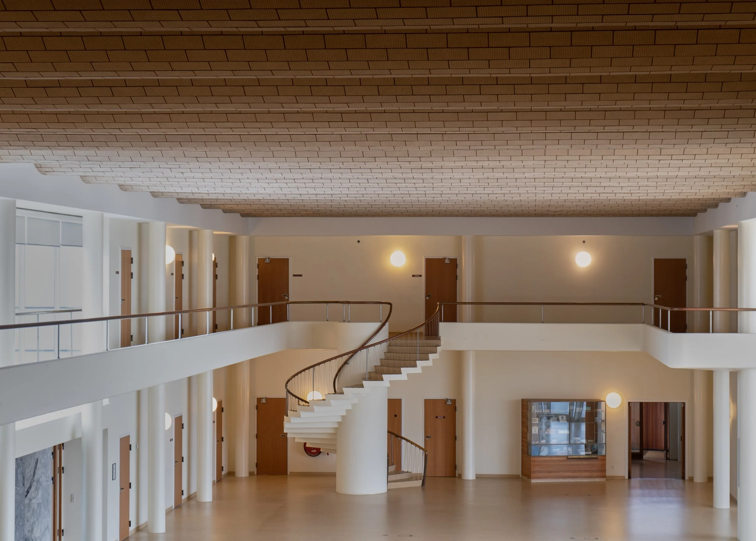 Interior architectural photography of a curved functionalist staircase at the Vilhelm Lauritzen Terminal under a structural brick ceiling. Shot using ambient light to document spatial design, authentic material textures, and quiet, intentional interi