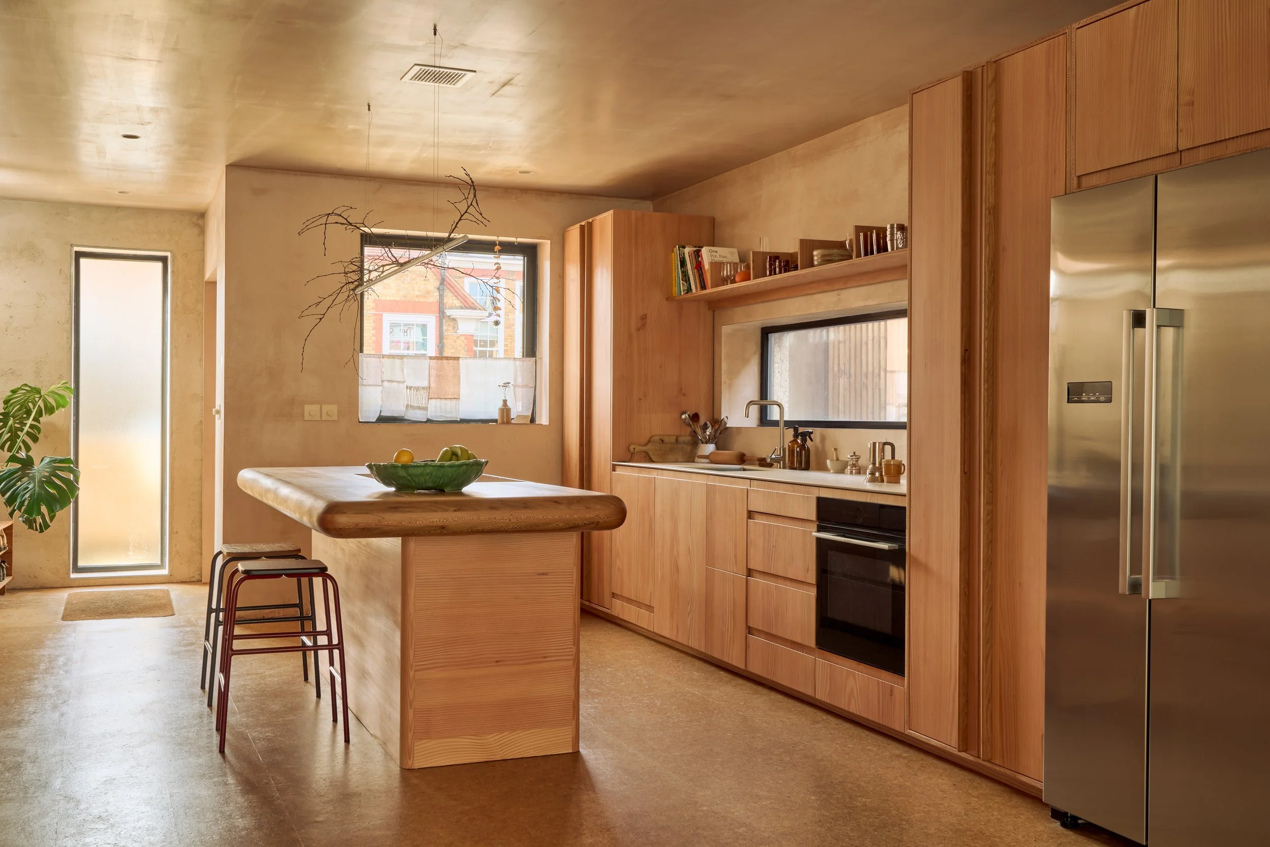 Sustainable modern kitchen in Nina's House featuring douglas fir cabinetry, a monolithic London plane wood island with rounded edges, and warm cork flooring. 