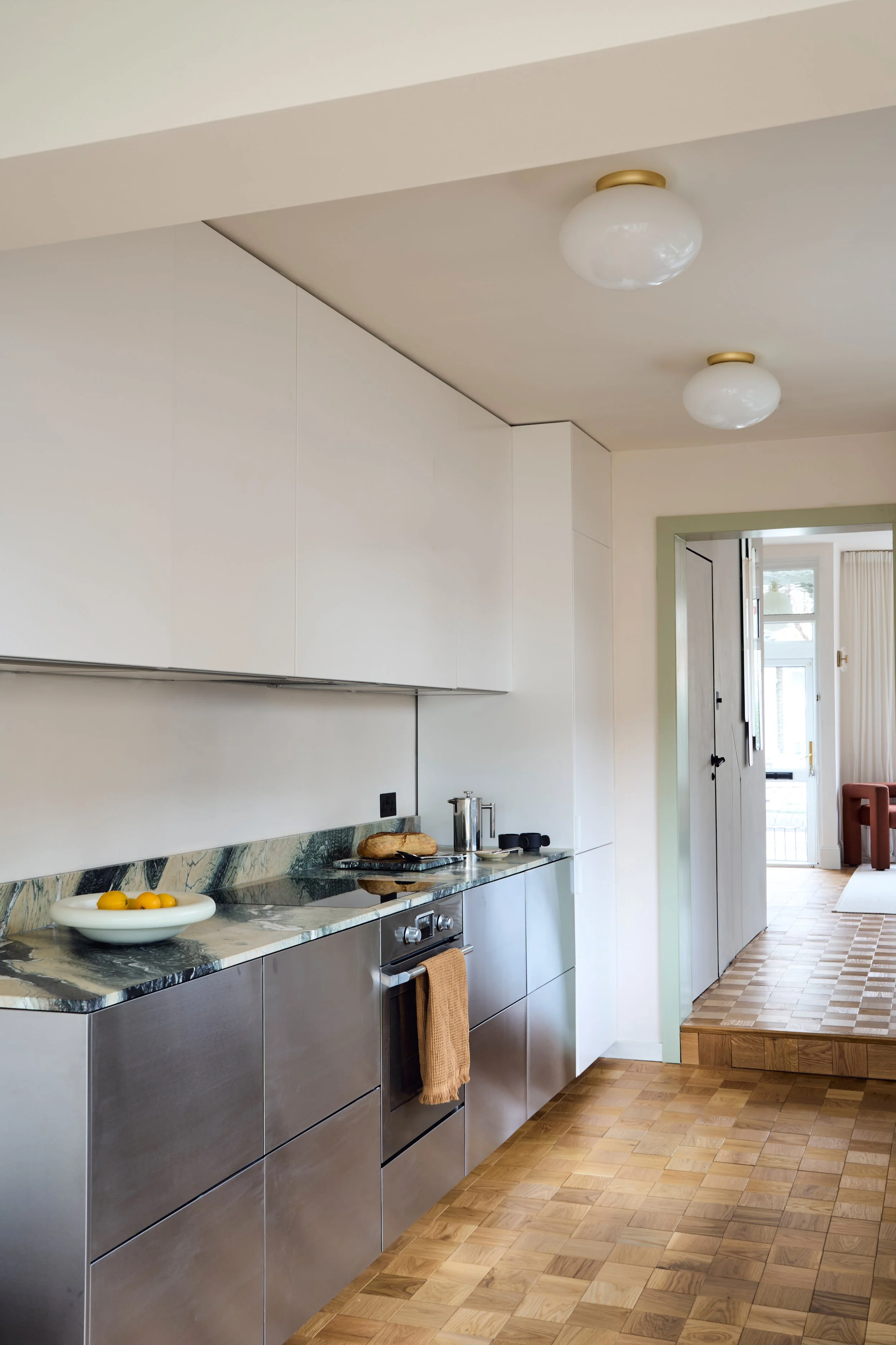 Modern minimalist kitchen featuring brushed stainless steel cabinets, a green marble countertop and backsplash, and light wood parquet flooring. 