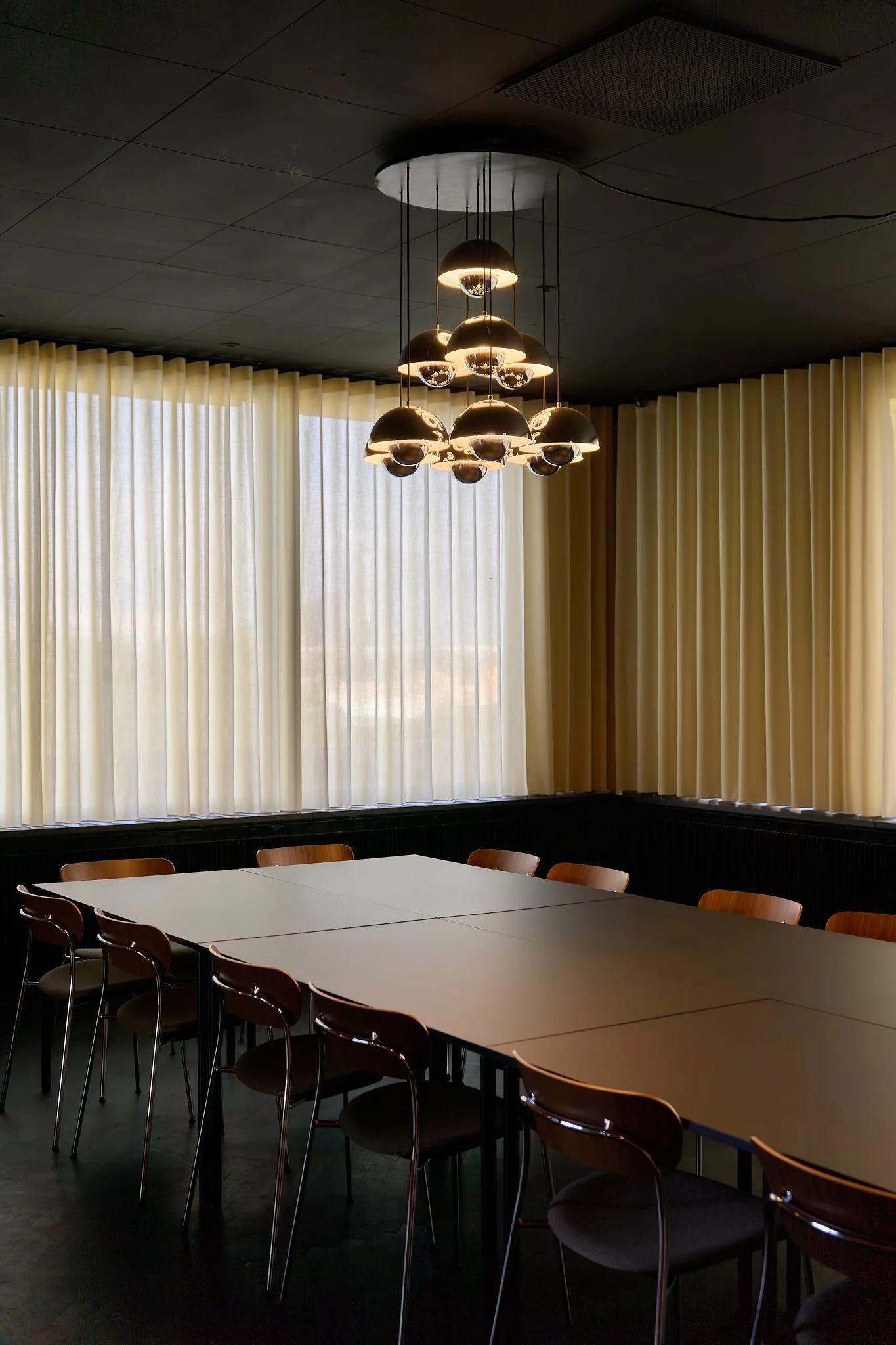 Interior architectural photography of a historic Danish boardroom curated with &Tradition furniture. Shot using natural available light to capture geometric patterns, clean mid-century lines, and an iconic Verner Panton lighting installation. 