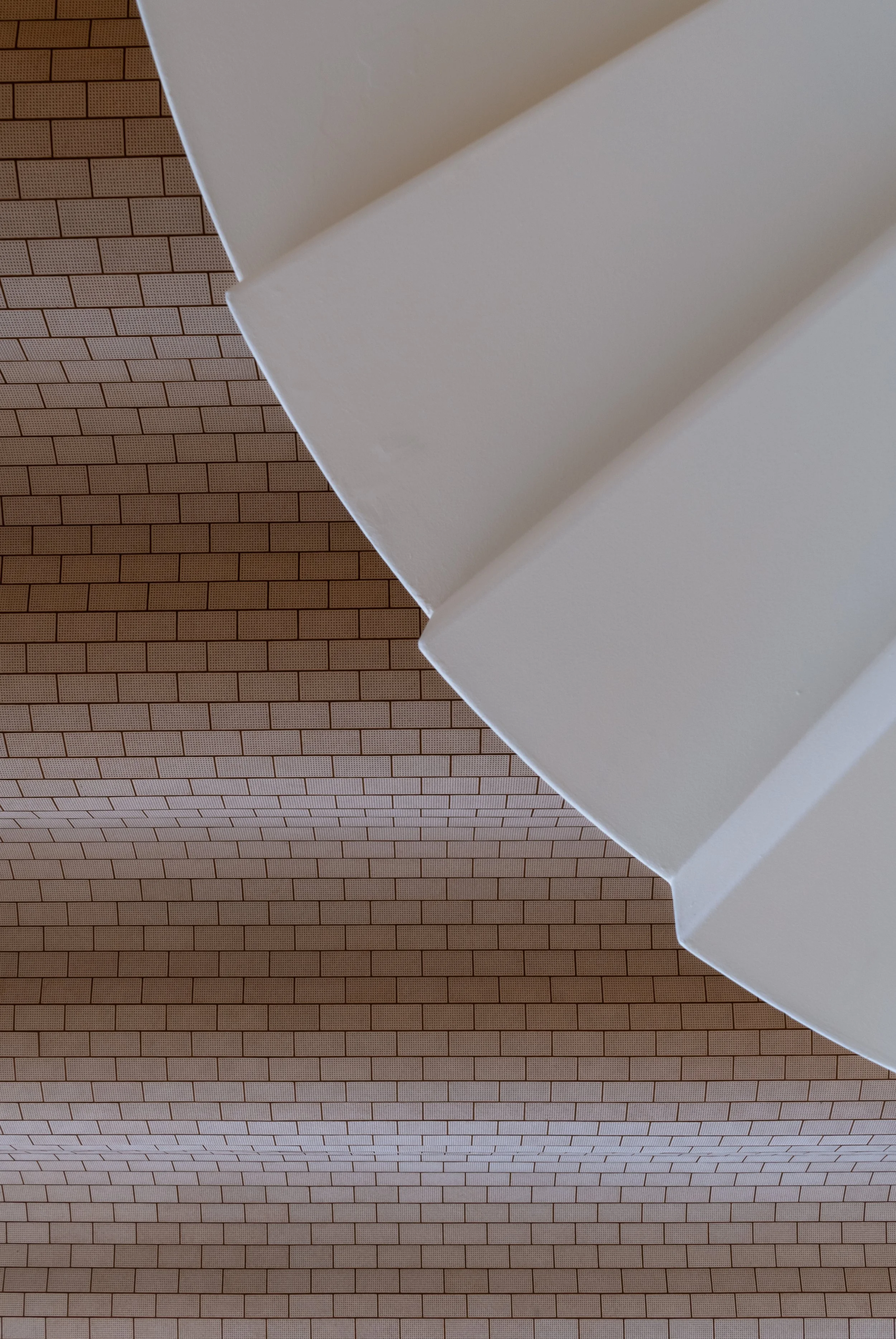 Architectural detail photograph from the Vilhelm Lauritzen Terminal, showcasing a graphic top-down perspective of a minimalist white staircase against the undulating brick ceiling. Shot using soft ambient light to emphasise geometric abstraction, mat