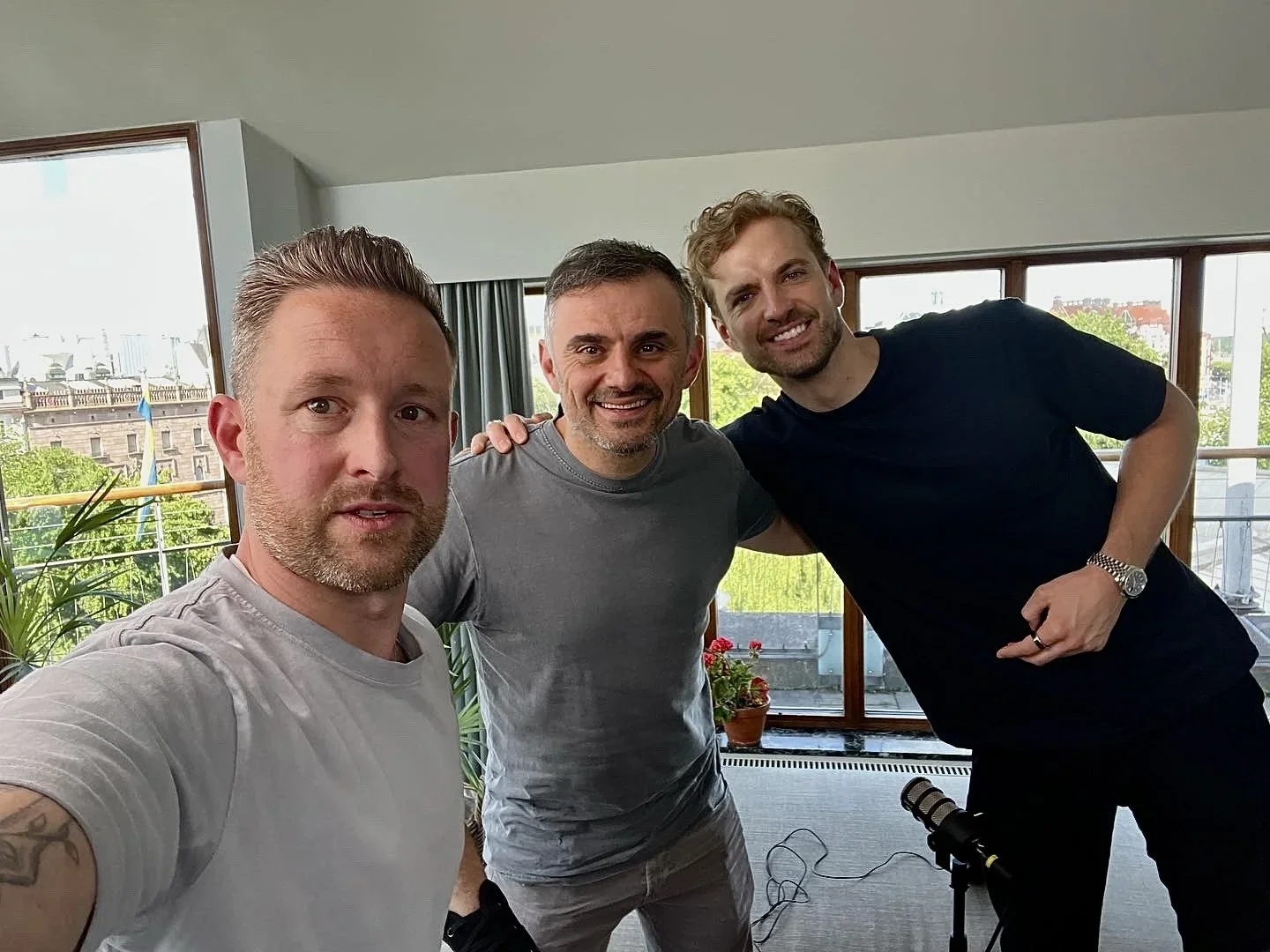 Four men smiling and posing for a selfie in a high-rise building with large windows revealing an urban cityscape in the background.