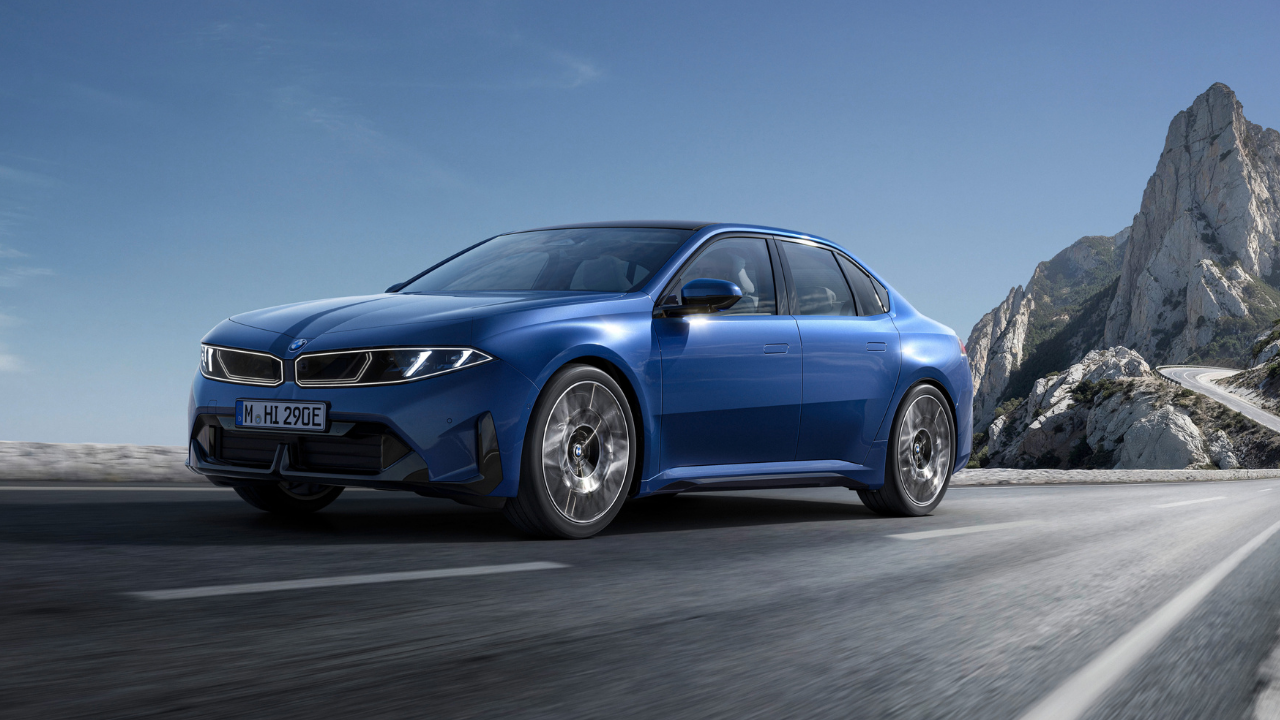 Blue BMW i350 electric luxury sedan driving dynamically on a winding coastal canyon road, showcasing BMW electric performance.