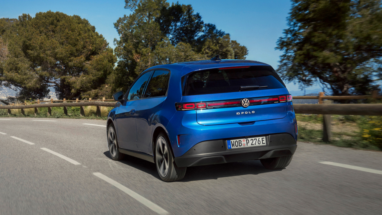 Rear view of blue Volkswagen ID. Polo driving past trees on sunlit road, featuring the id polo ev badge.