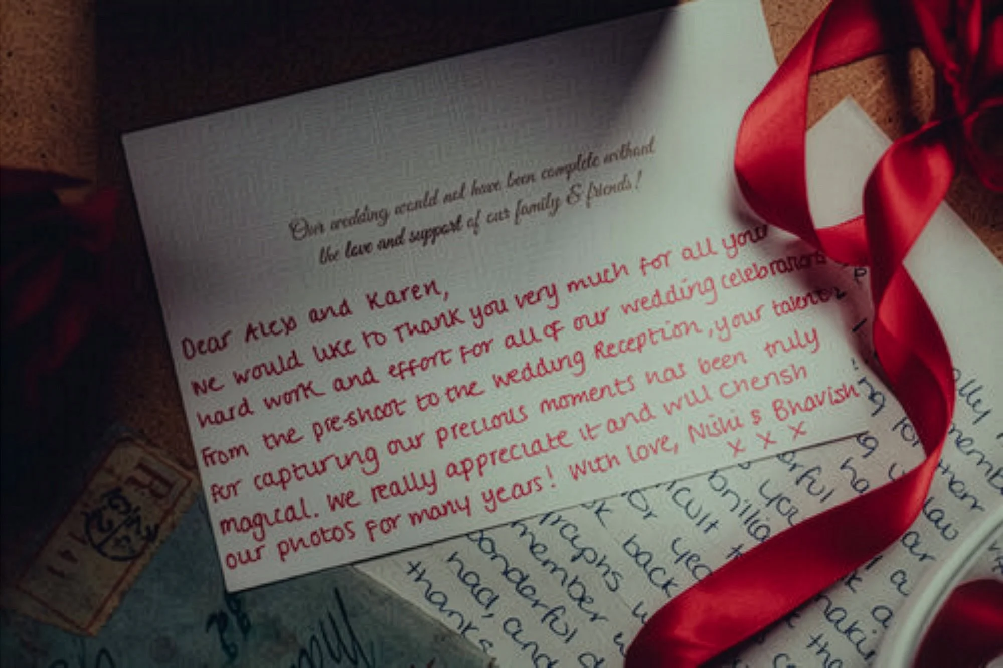 Close-up of a handwritten thank you note on white paper with a red ribbon, on top of a book with handwritten text.